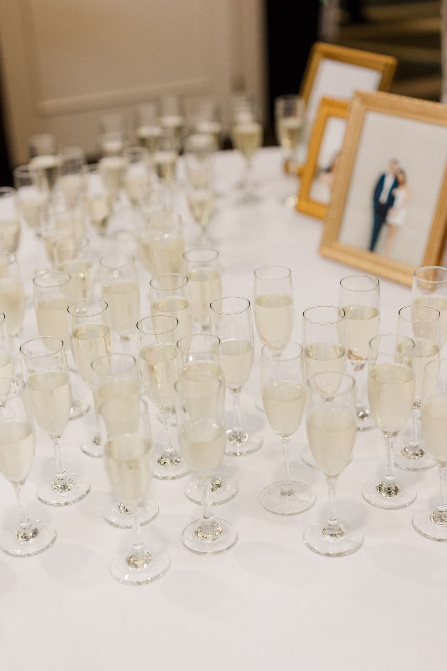 Champagne flutes filled with sparkling wine arranged on a white tablecloth beside a framed wedding photo.