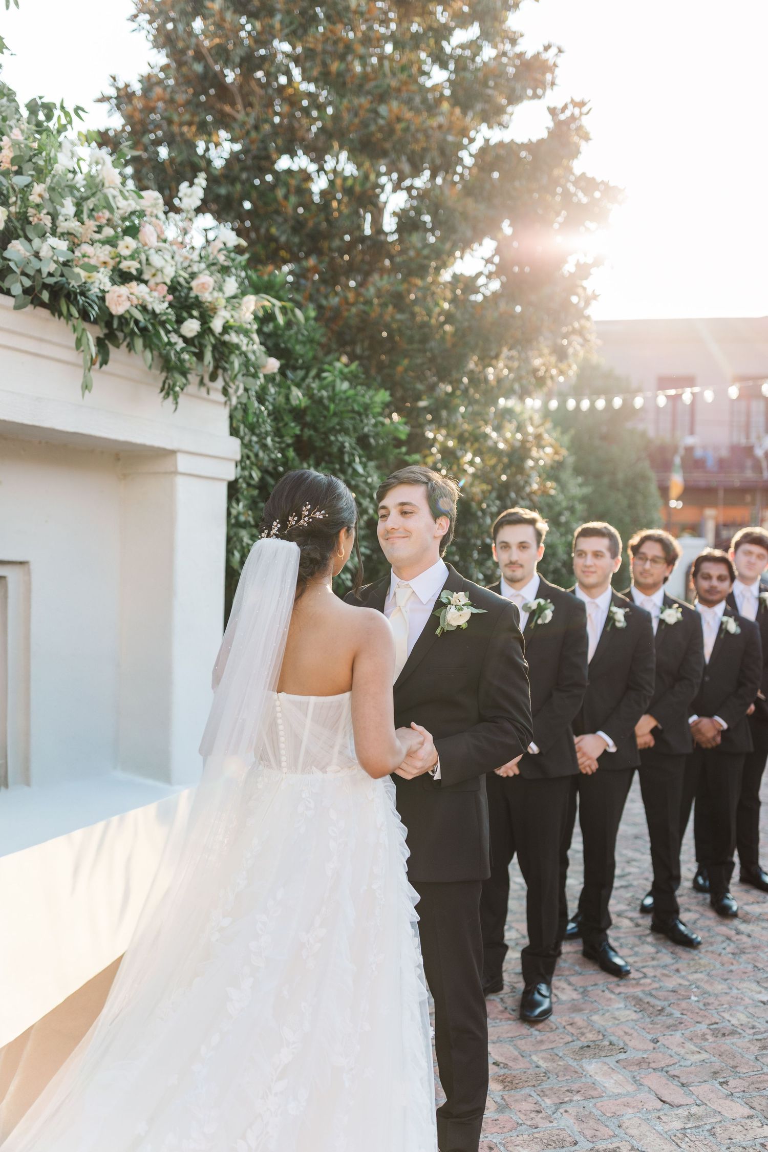 Couple exchanges vows during outdoor ceremony as groomsmen look on.