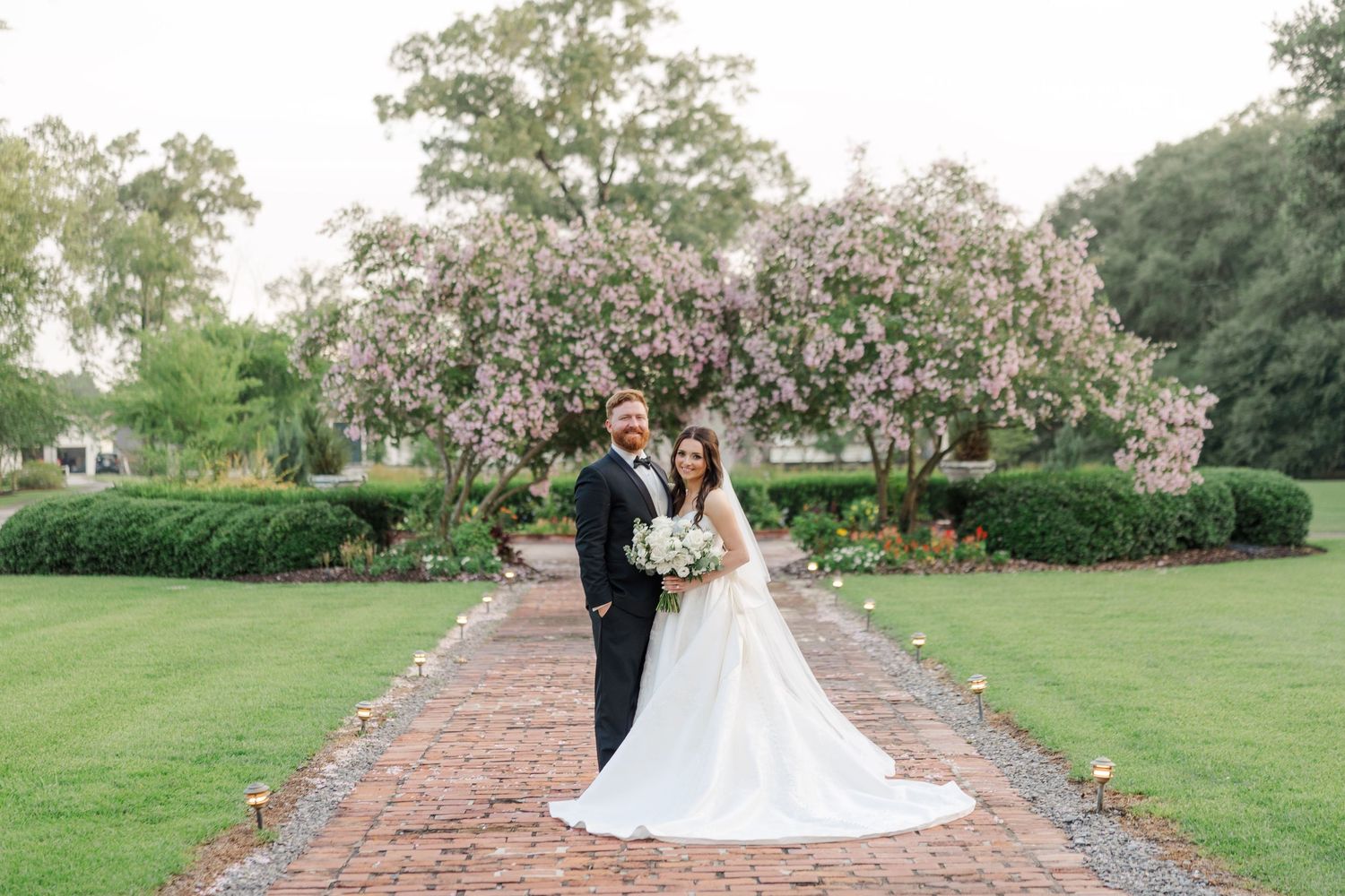 Wedding ceremony setup with pink flowering trees lining a brick pathway.
