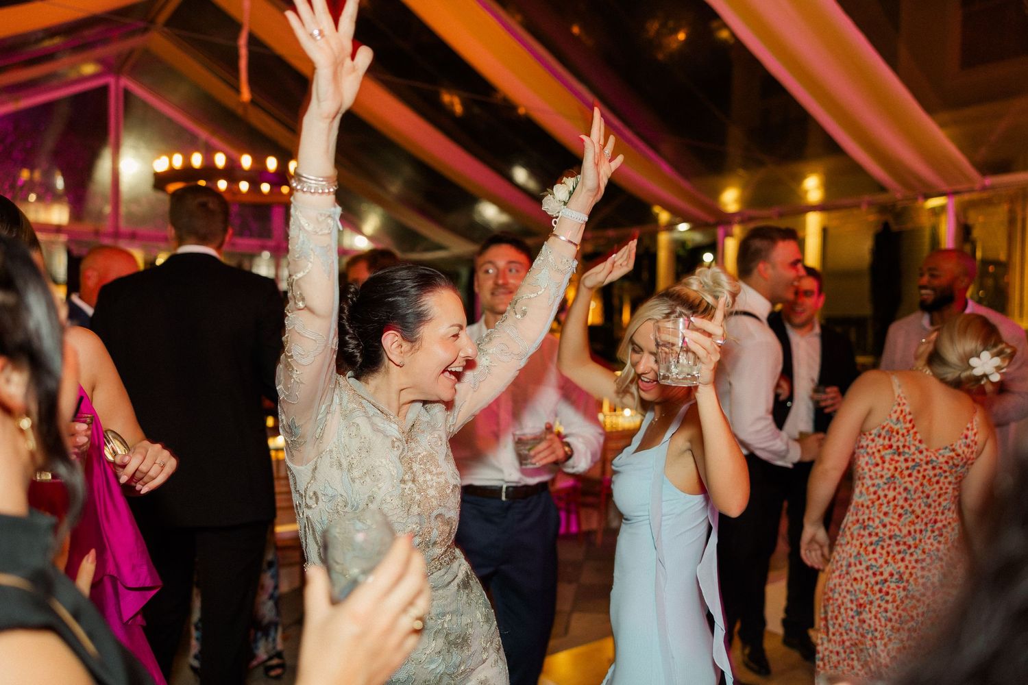 Wedding guests dancing with raised arms during lively reception celebration.