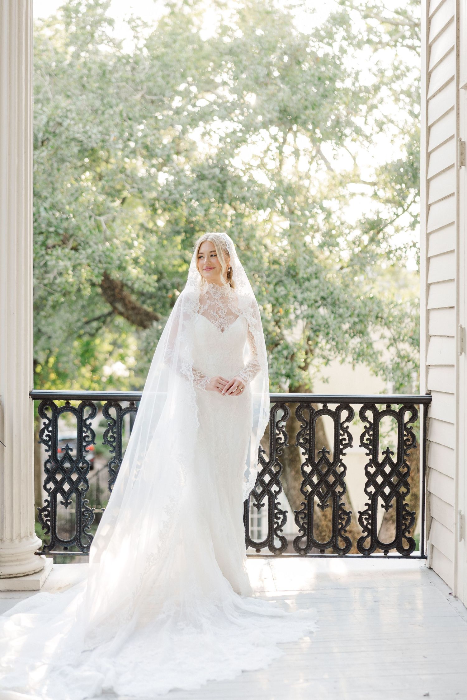 A flowing white wedding dress displayed on an elegant white veranda with ornate black railings.