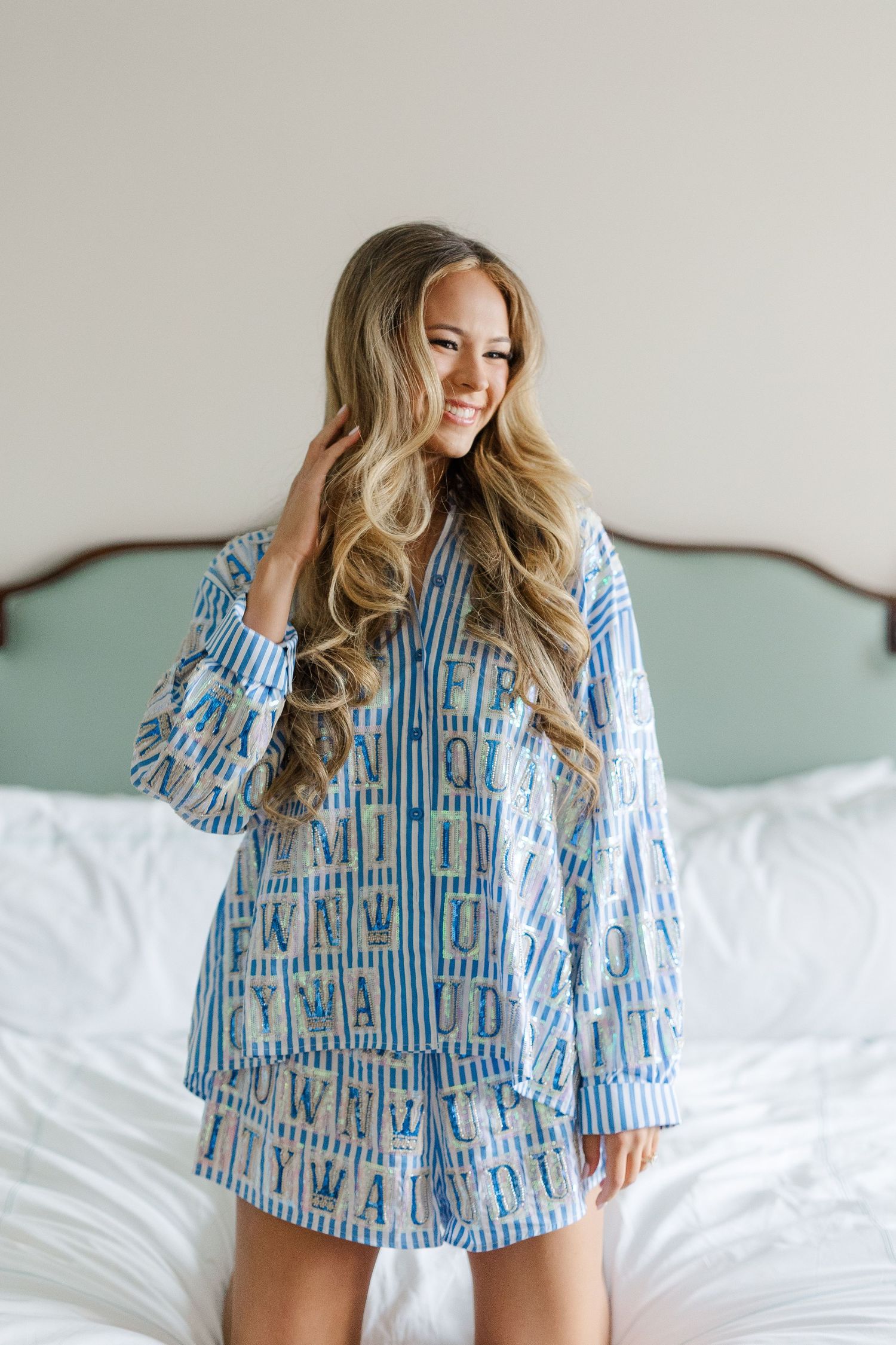 A person in blue and white striped pajamas sits on a white bed while posing in different playful positions.