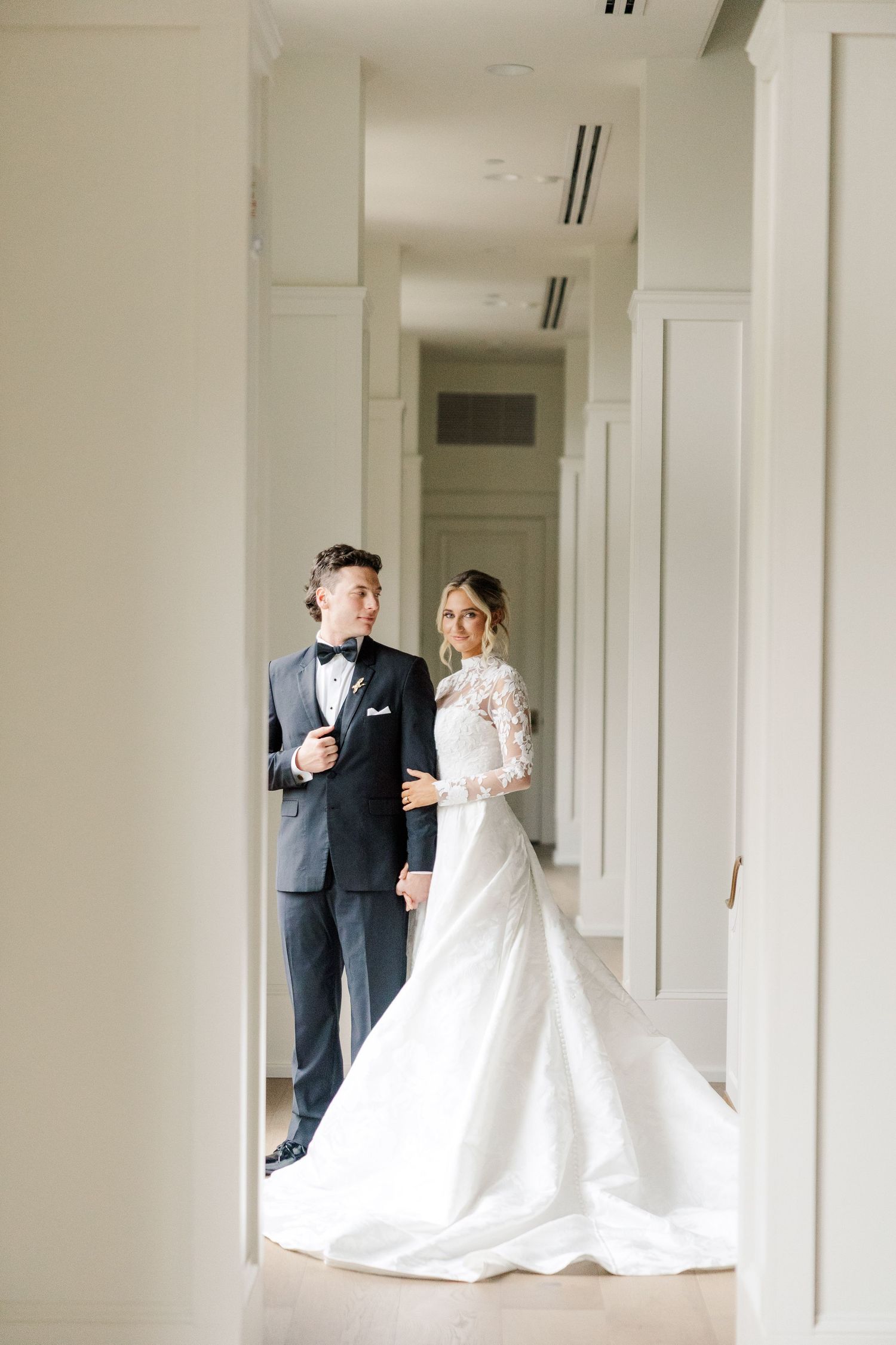 Wide hallway first look photos capturing tender moments between newlyweds in white and formal attire.