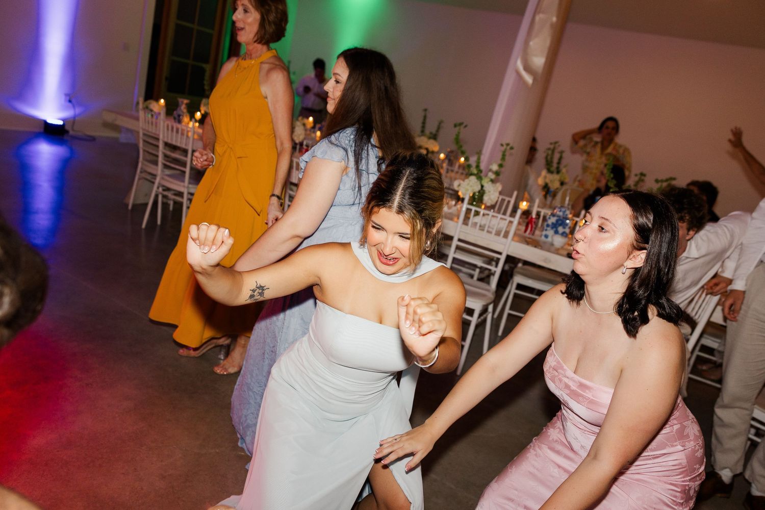 Bridesmaids in blue and pink dresses dance joyfully together at lively wedding reception on the dance floor.