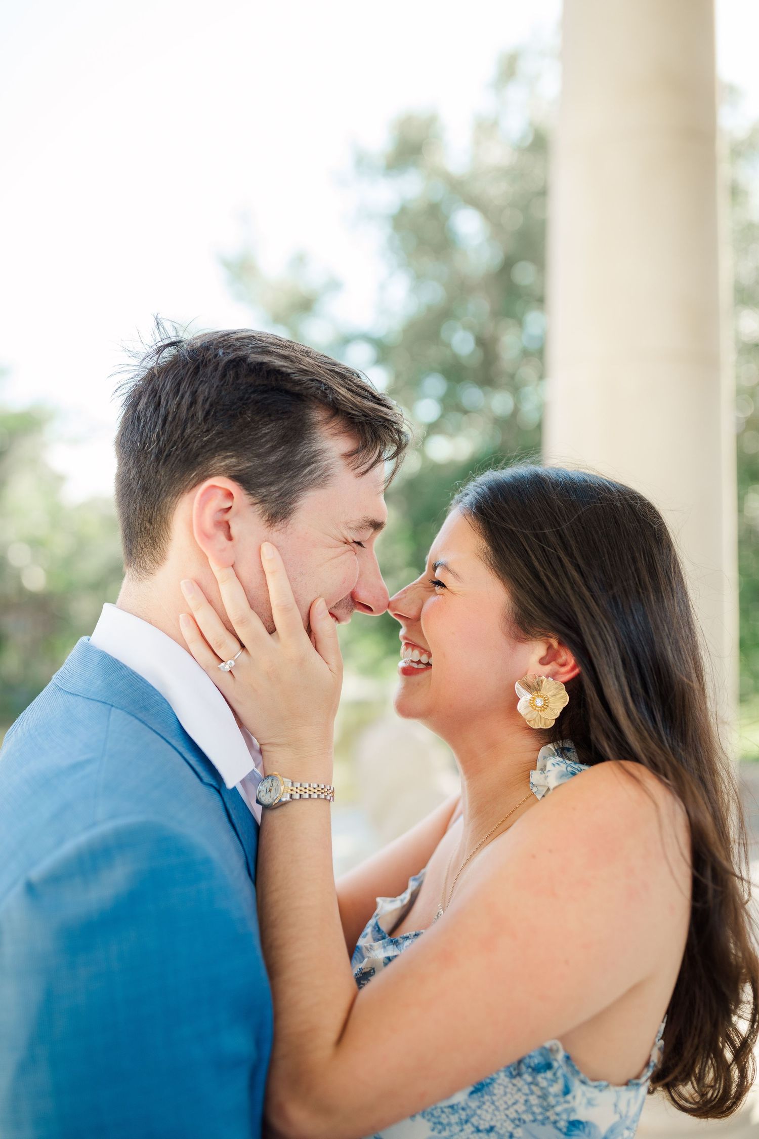 A tender romantic moment shared under grand white columns in soft natural light.