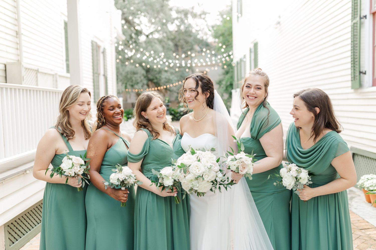 Bridesmaids in matching seafoam green dresses pose with bride in white gown holding elegant white bouquets.