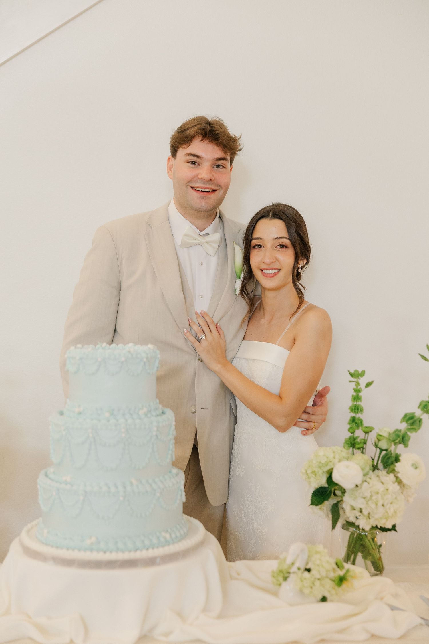 Smiling bride and groom posing beside a three-tier light blue wedding cake with floral decorations.
