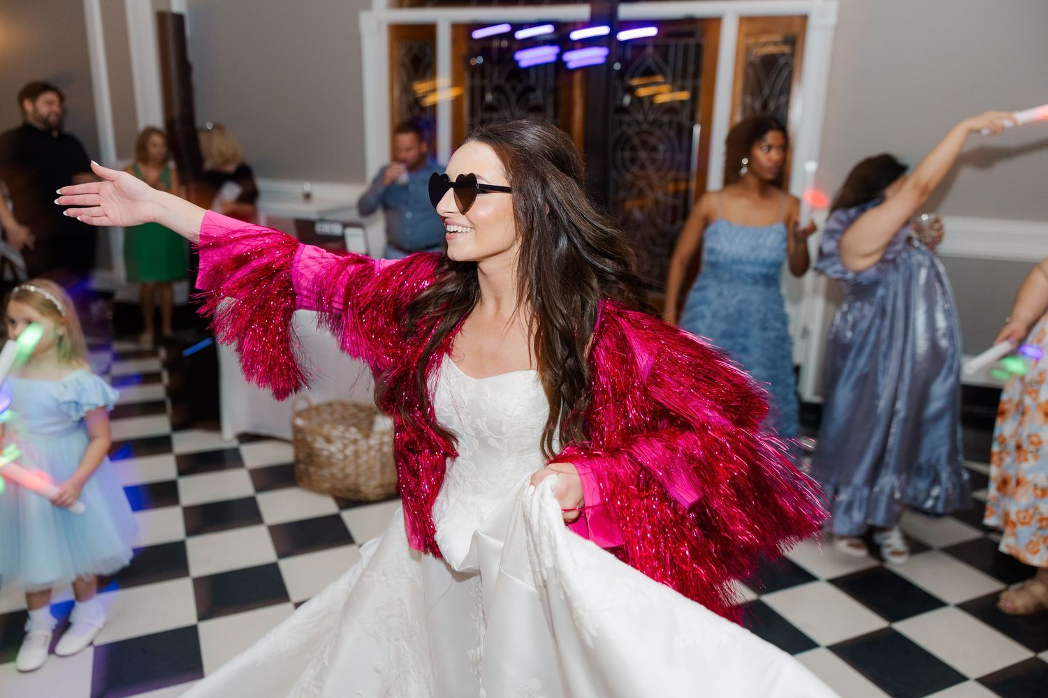 Wedding guests dancing with person in red sequin jacket on checkered floor.