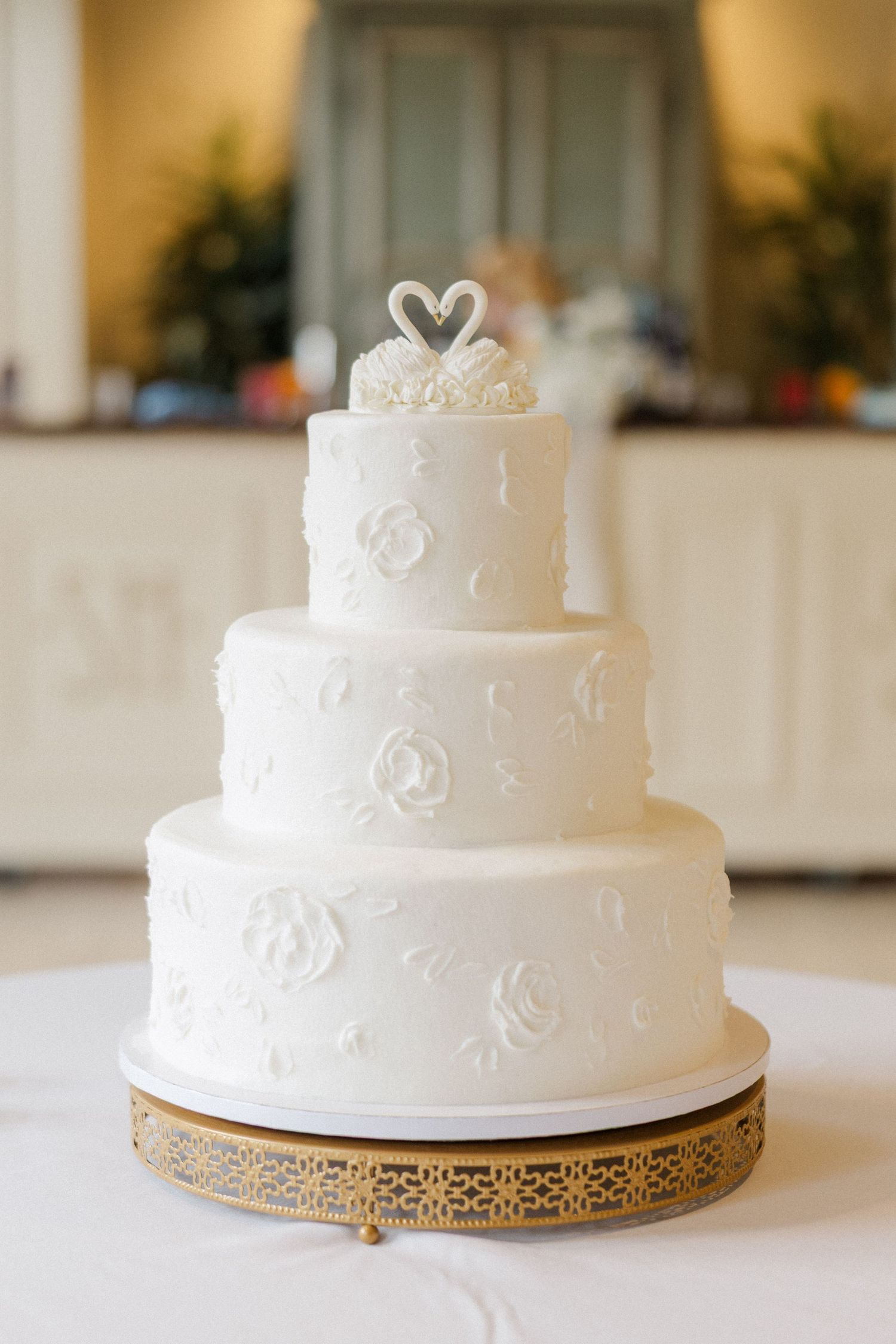 Elegant white wedding cake with delicate floral details displayed on a decorative gold stand.
