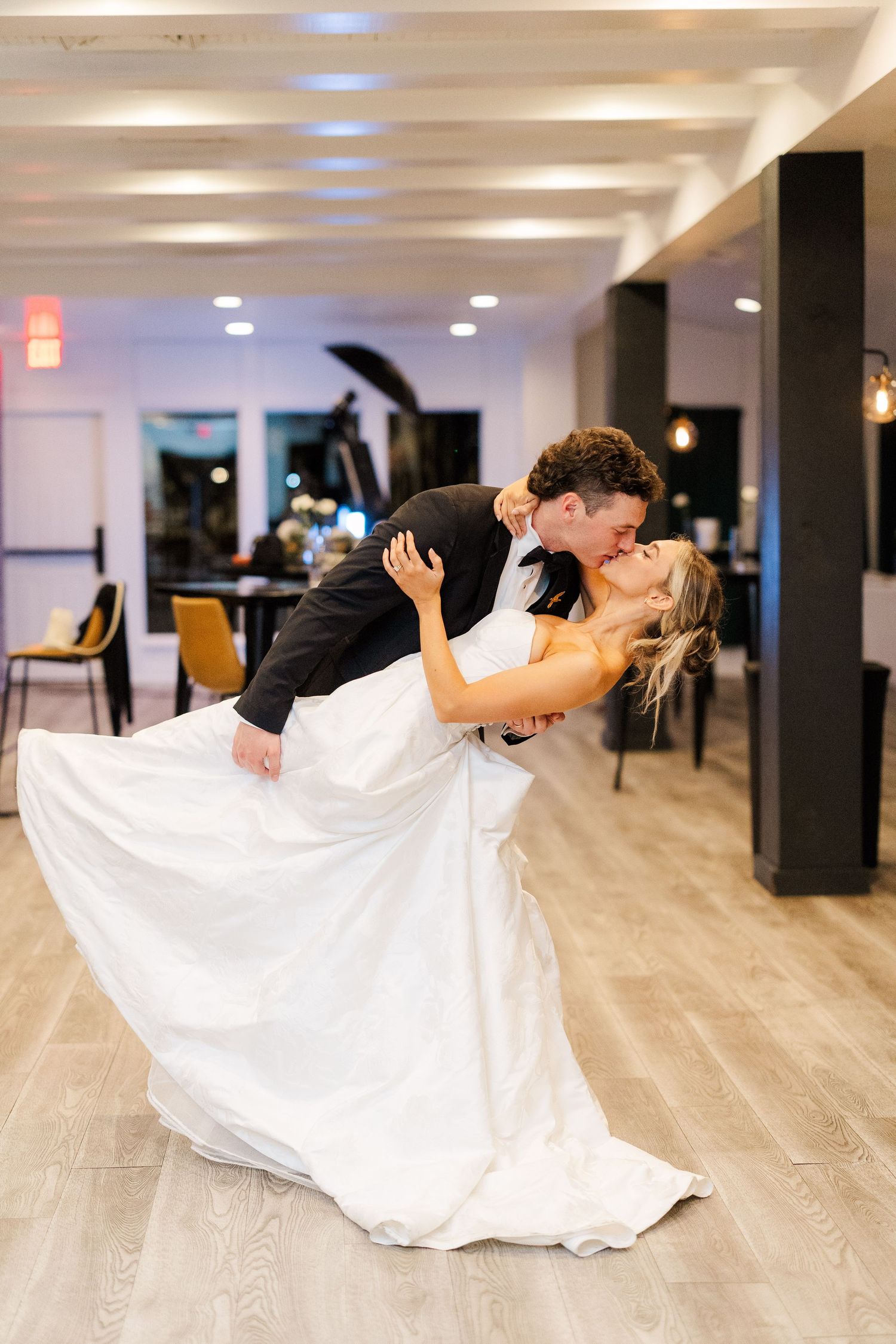 Romantic wedding dance dip on a light wooden floor in an elegant indoor venue.
