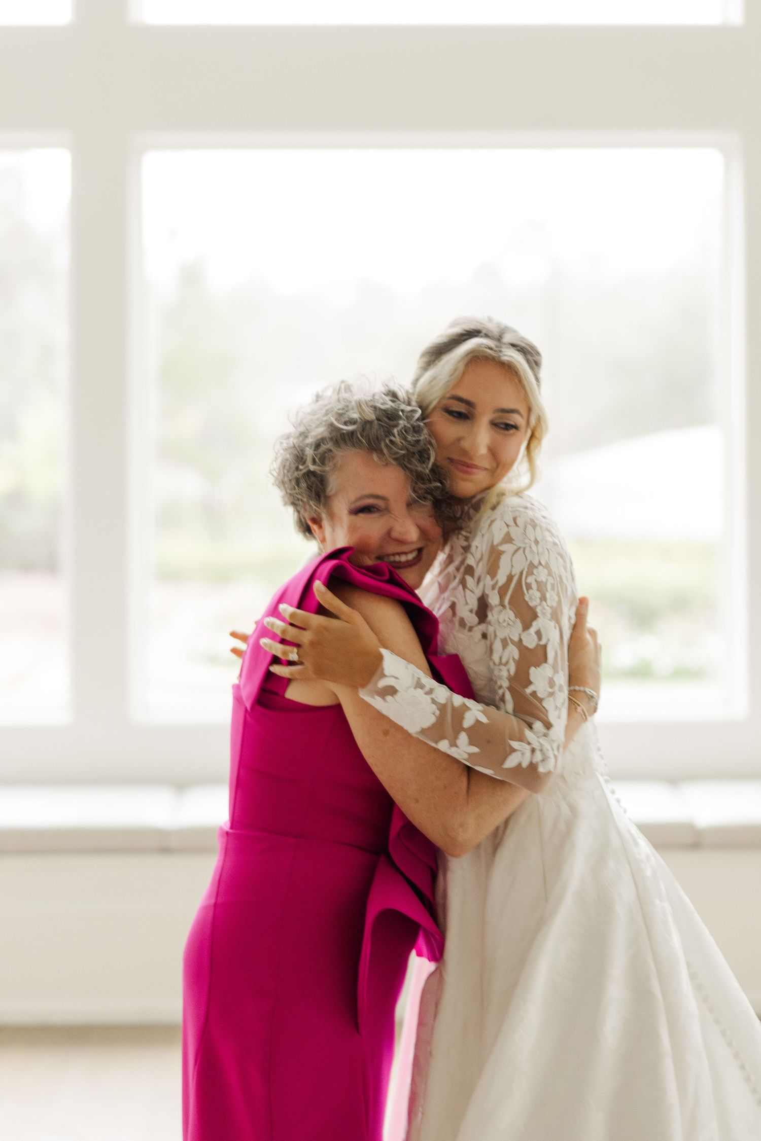 Emotional moment captured as two people embrace in a bright sunlit room with white decor.