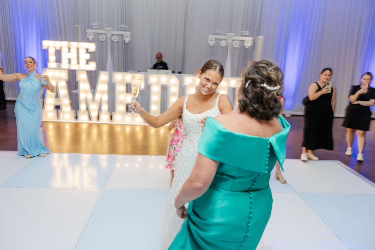 Reception venue features elegant white draping, blue lighting, and illuminated signage.