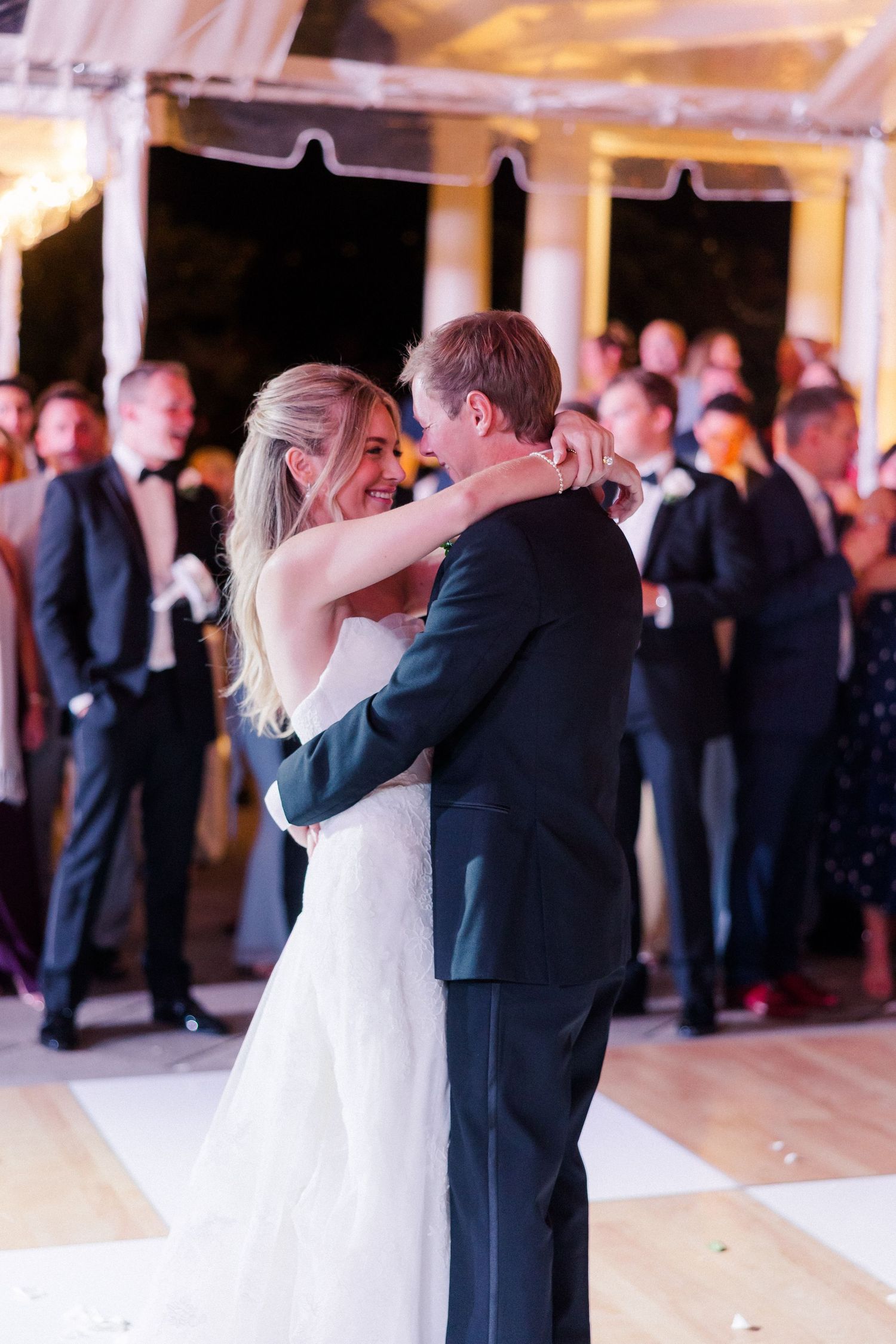 Wedding couple shares their first dance surrounded by guests at an elegant indoor reception.
