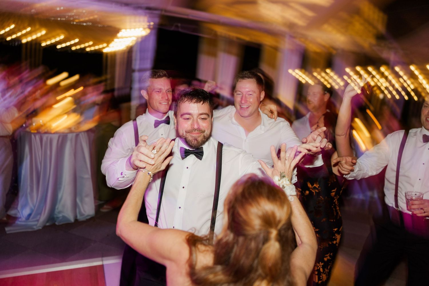 Lively dance floor scene at wedding reception with colorful lighting and celebrating guests.
