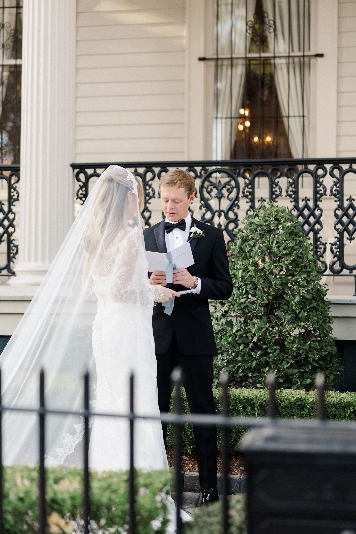 Couple reading vows during outdoor ceremony on porch with white columns.