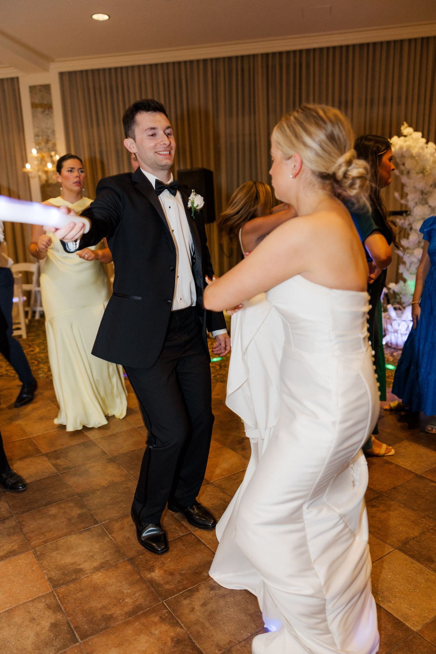 A couple dances together at their wedding reception on a tiled floor surrounded by guests.