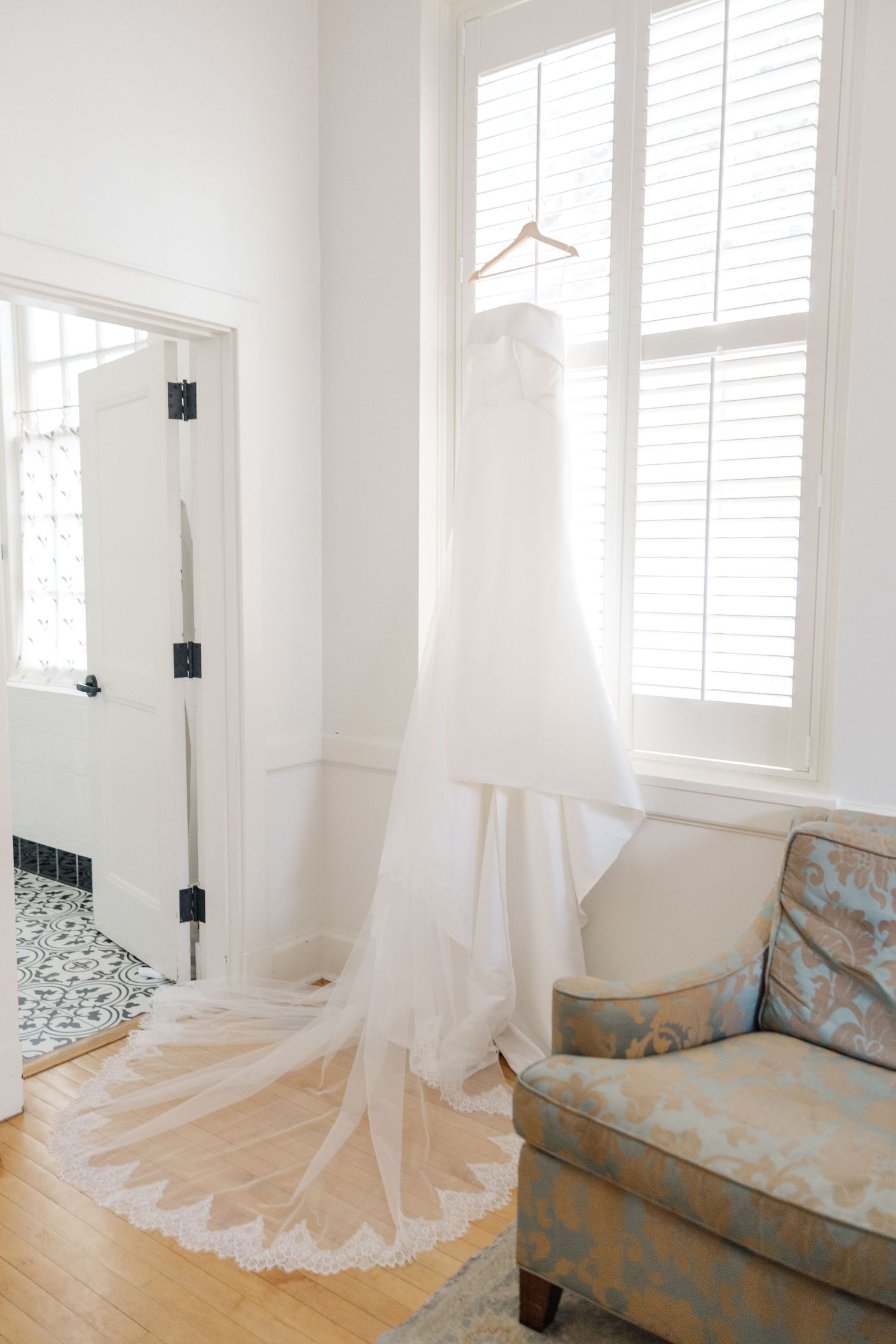 Elegant white wedding dress displayed against a light-filled window with soft draping details.
