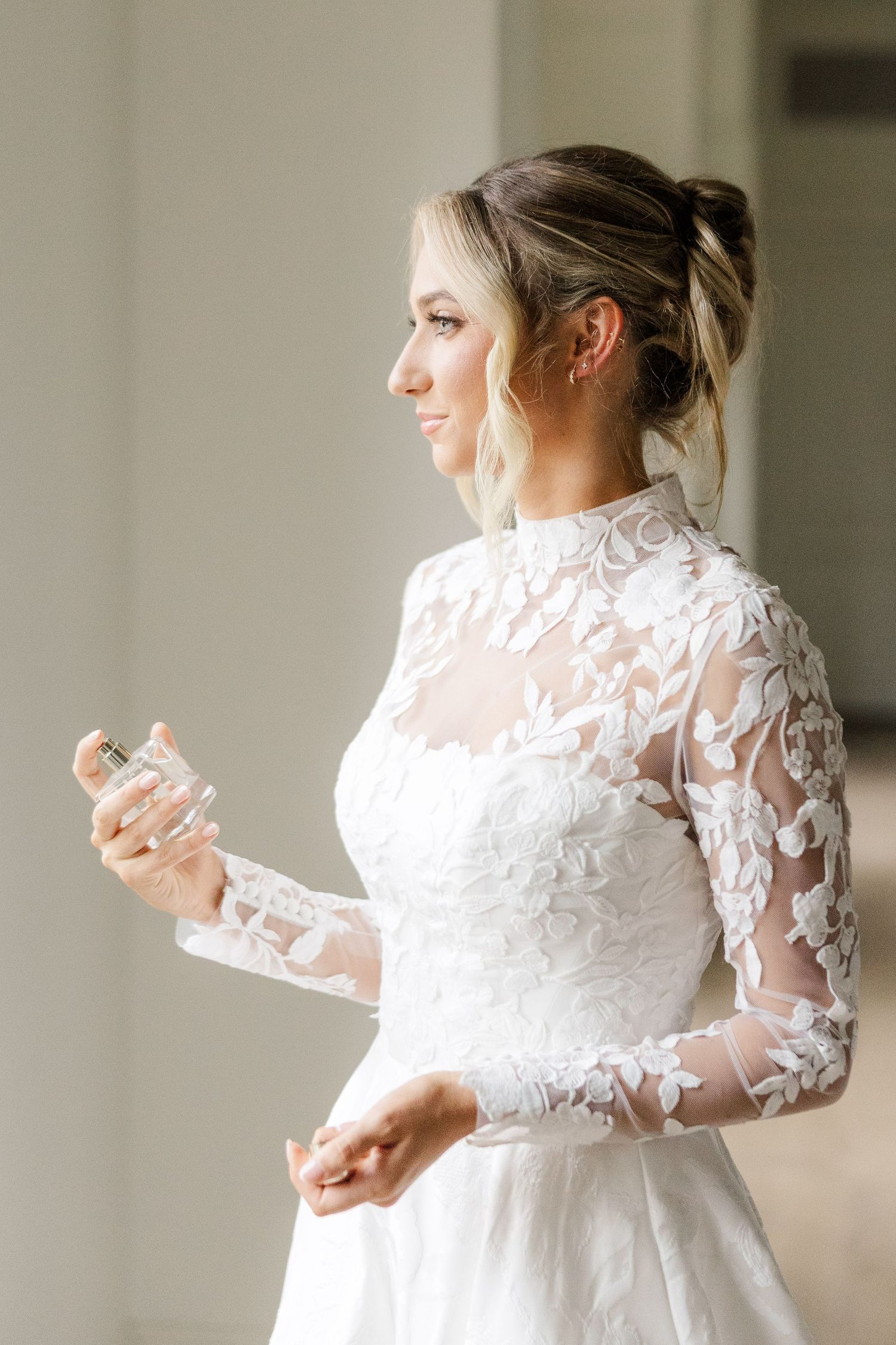 Bride in long sleeve lace wedding dress poses elegantly in natural window light.