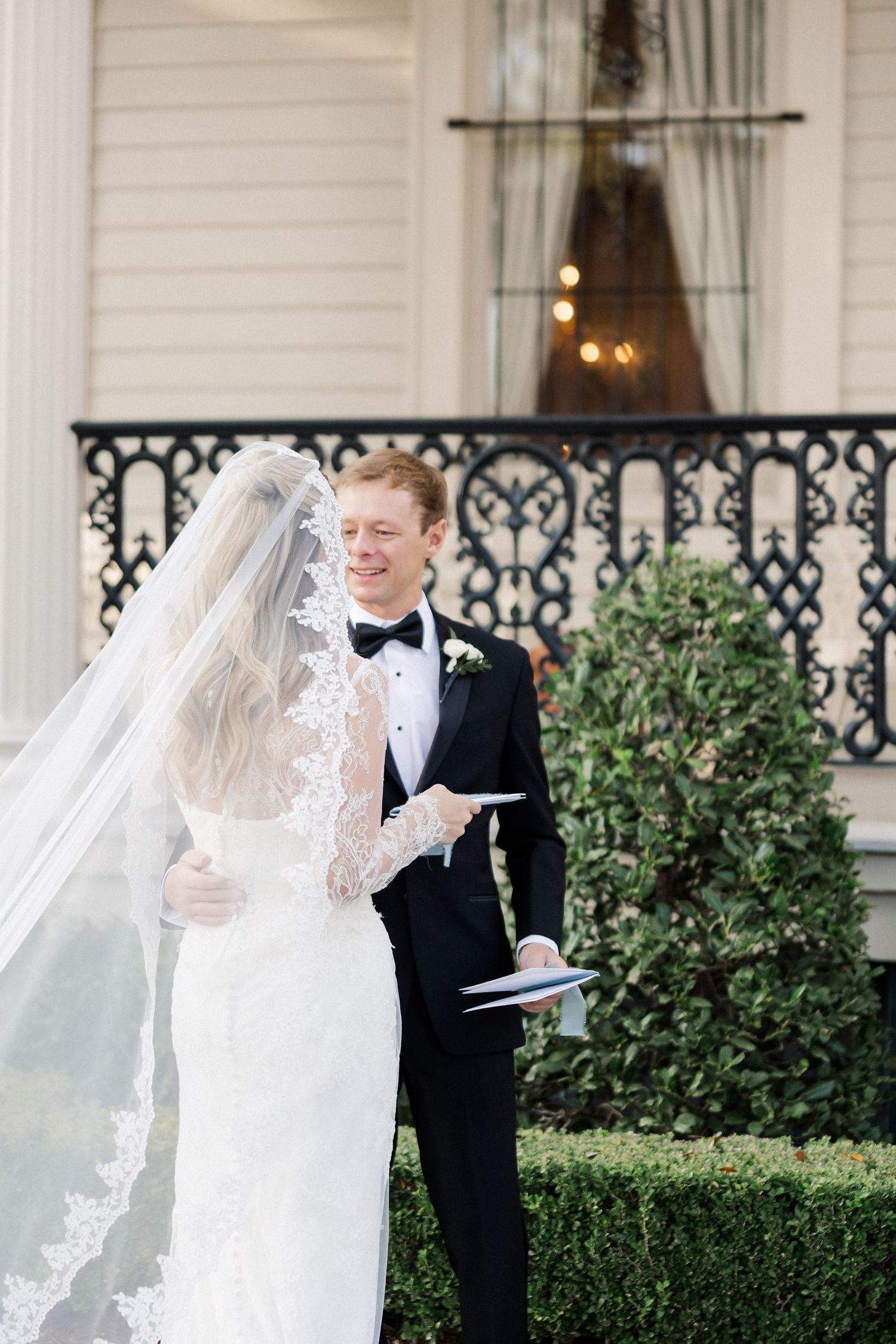 Elegant wedding couple sharing a moment on a white columned porch with greenery.