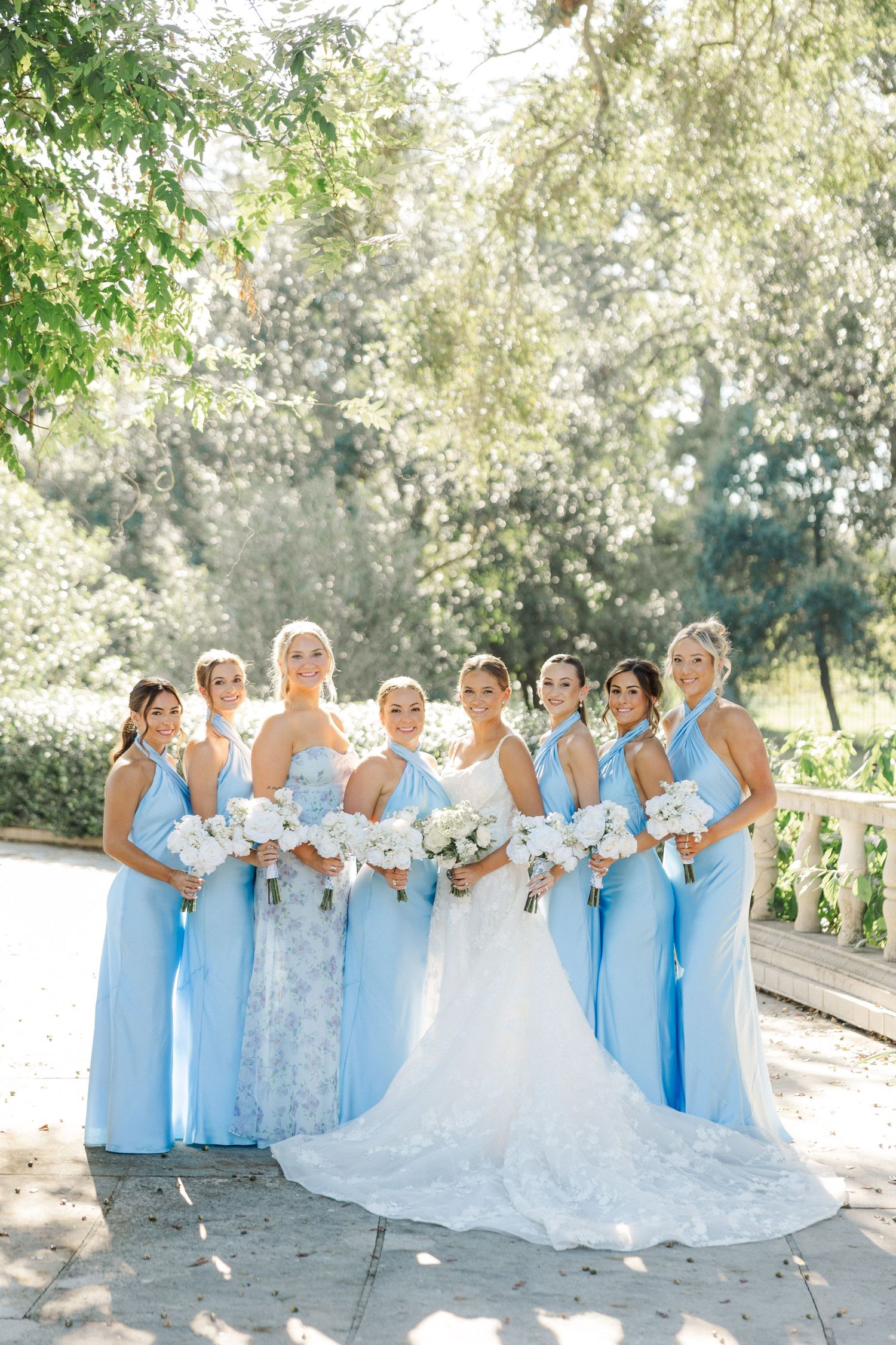 Bridal party in light blue dresses posing together outdoors with white bouquets.