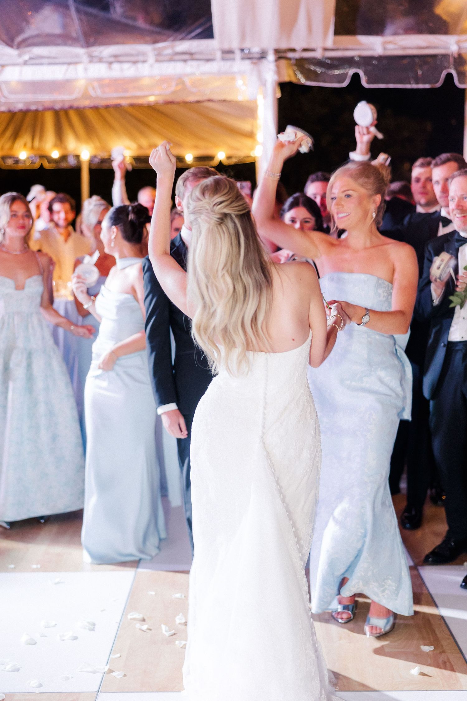 Wedding guests dancing and celebrating on a brightly lit dance floor at an evening reception.