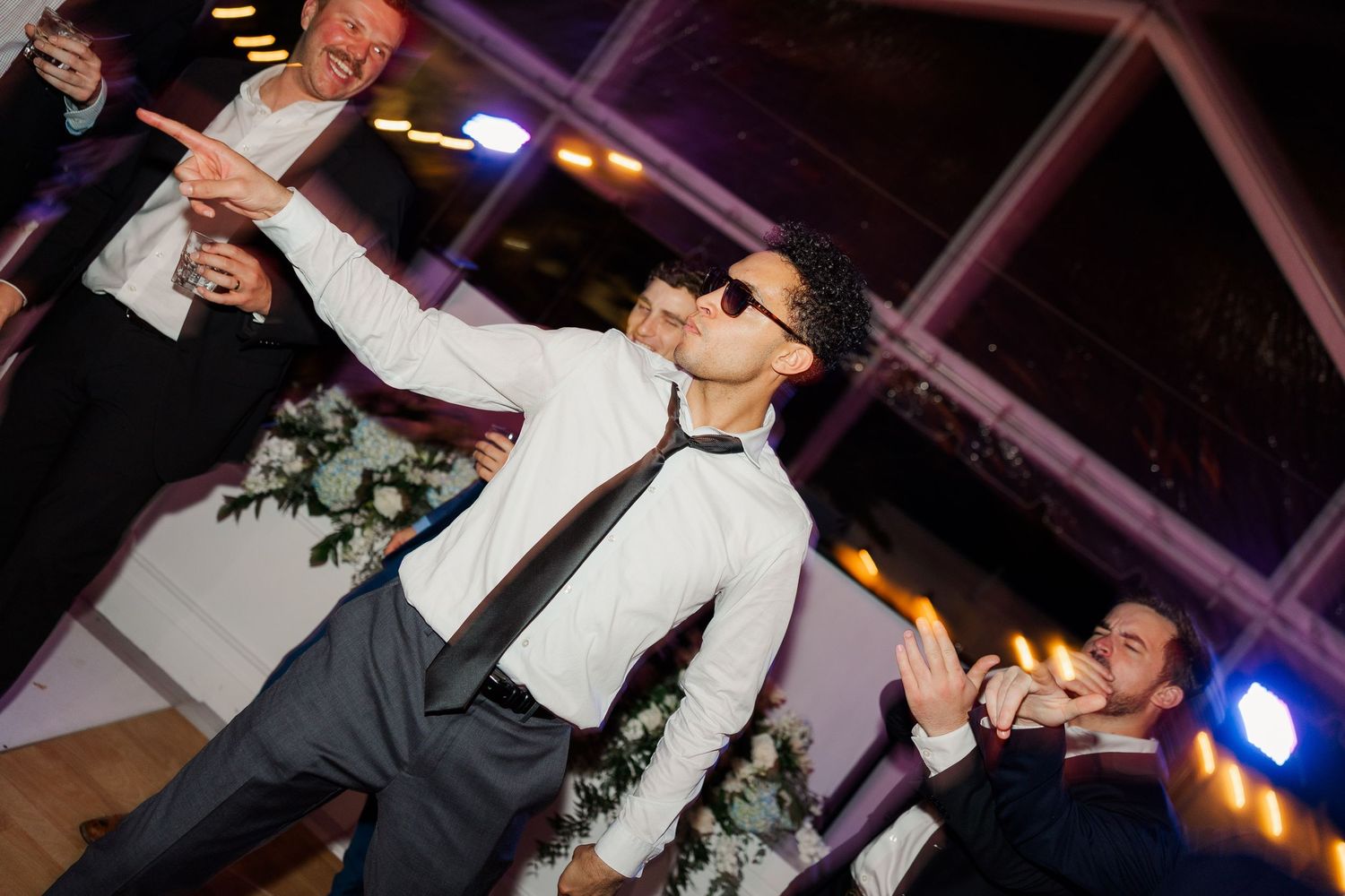Wedding reception dance party with energetic dancing under purple lighting.