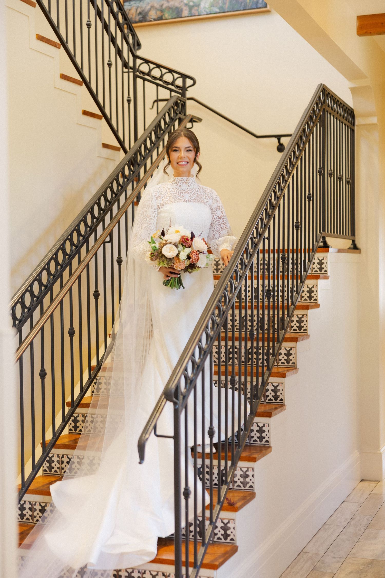 A flowing white wedding dress cascades down an elegant staircase with ornate iron railings and wooden steps.