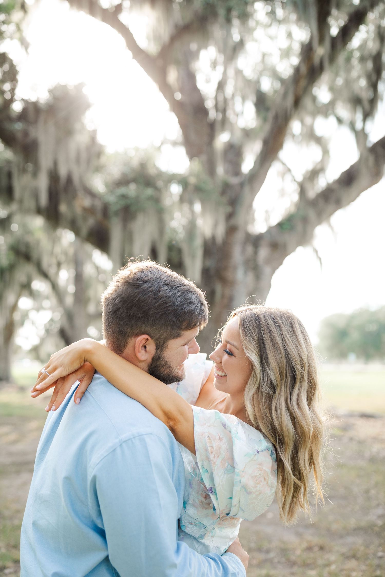 A romantic couple embraces under moss-draped oak trees in a dreamy outdoor setting.