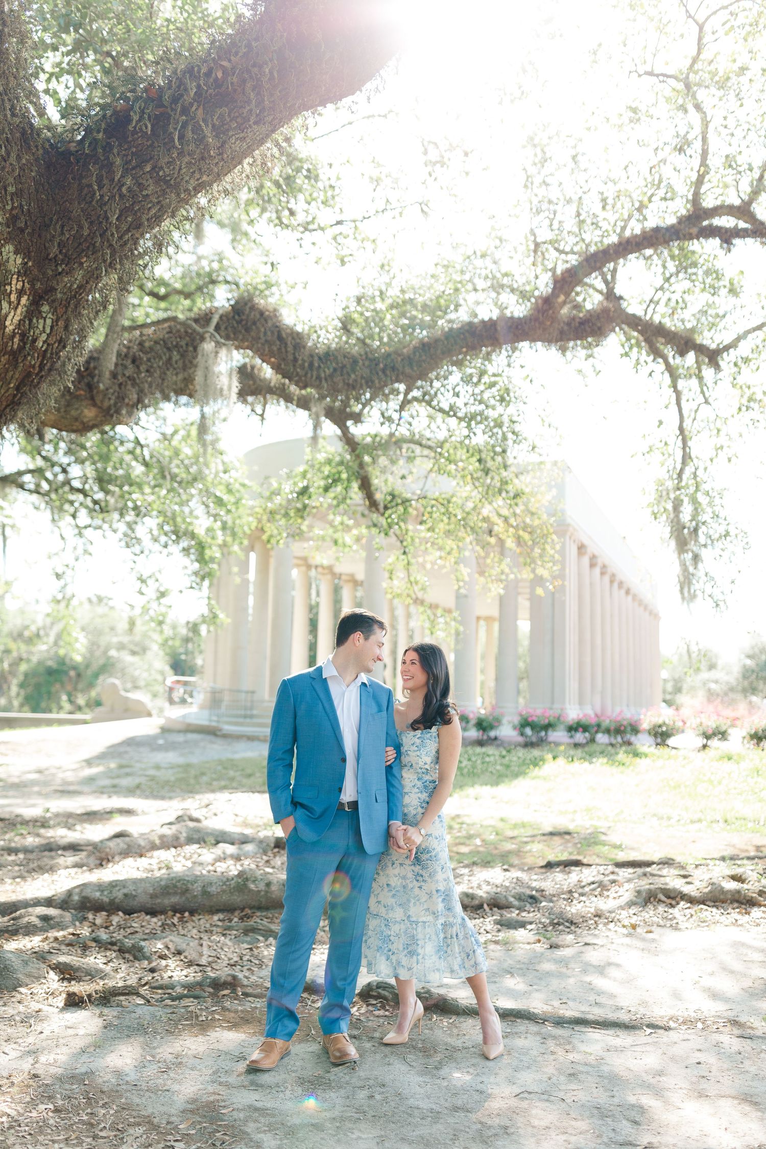 A romantic couple stands beneath a large oak tree on a sunlit path at a historic Southern estate.
