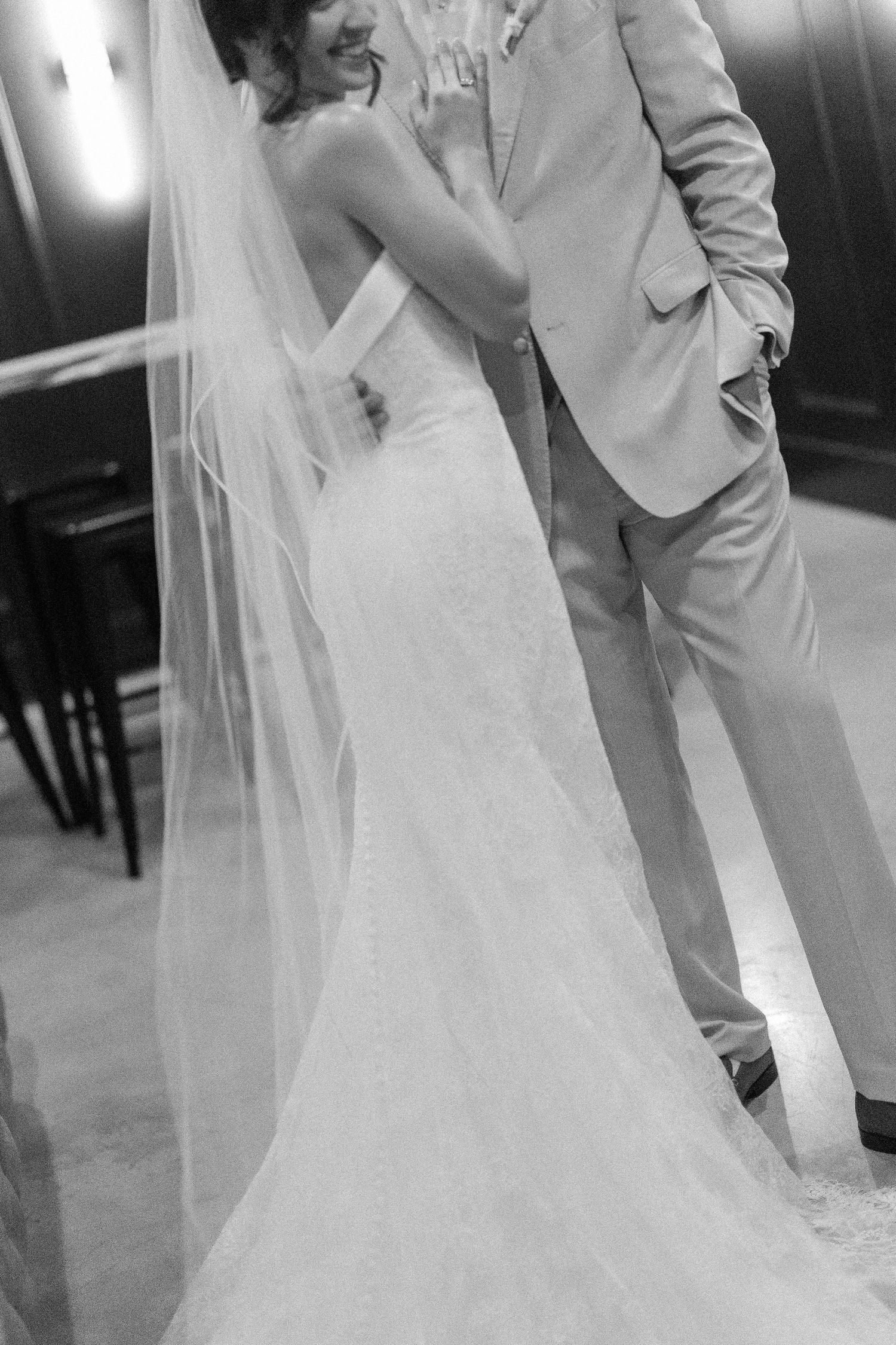 Black and white photo of bride in lace gown and groom in tan suit sharing first dance.