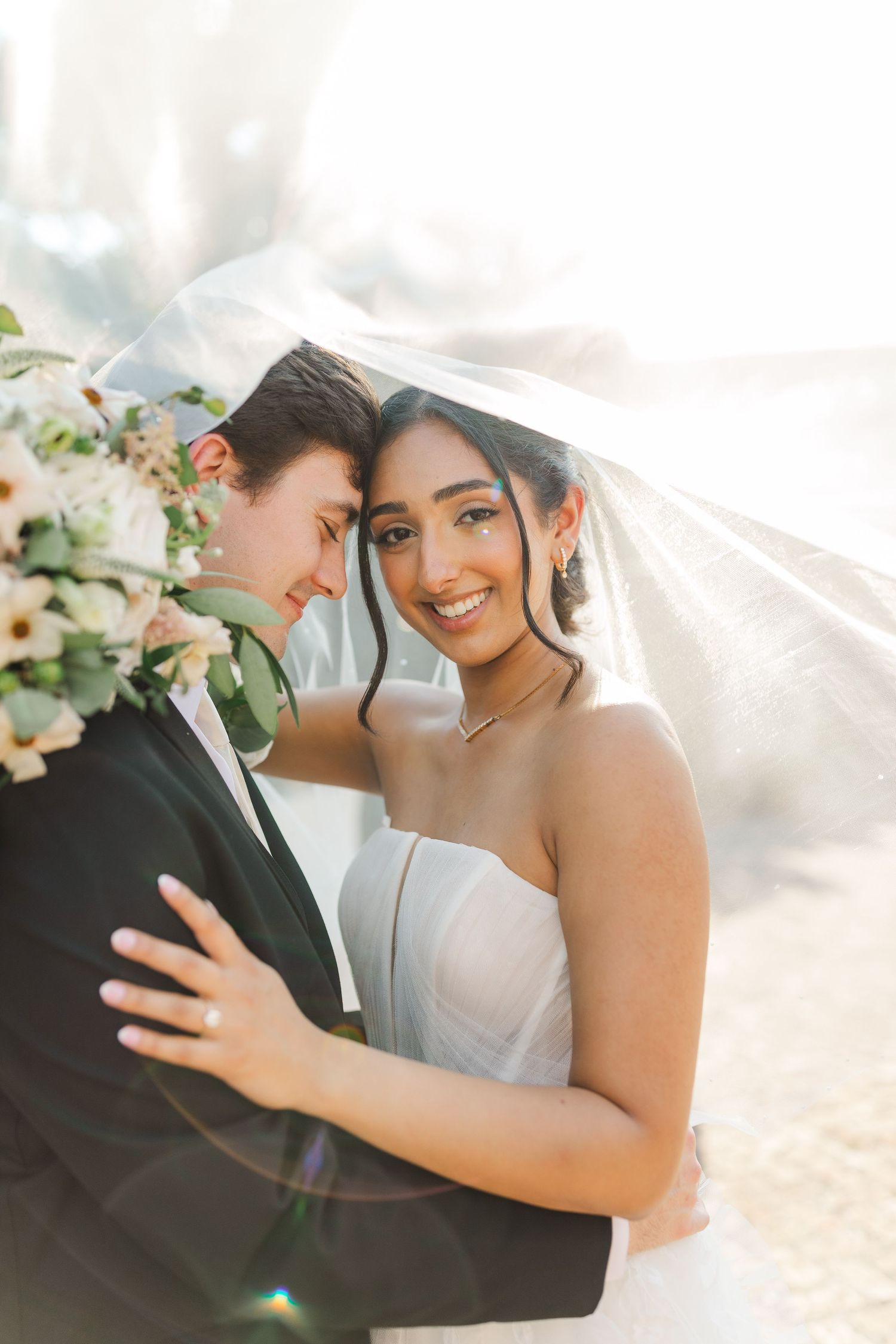 A romantic wedding photo with sunlit veil and delicate floral details in soft lighting.