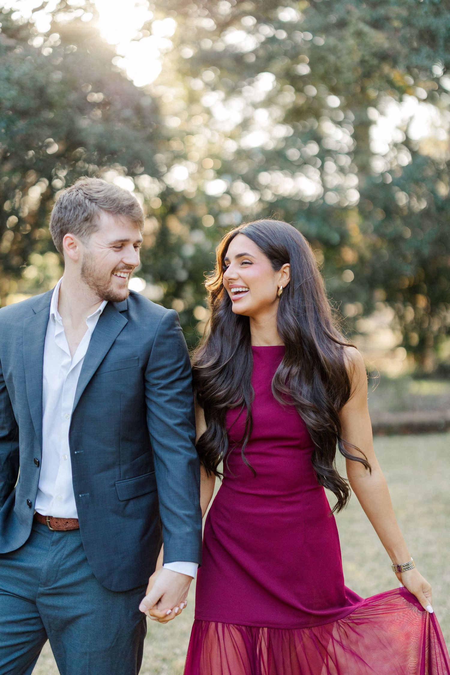 A joyful couple shares laughter while walking together in a sunlit garden setting.