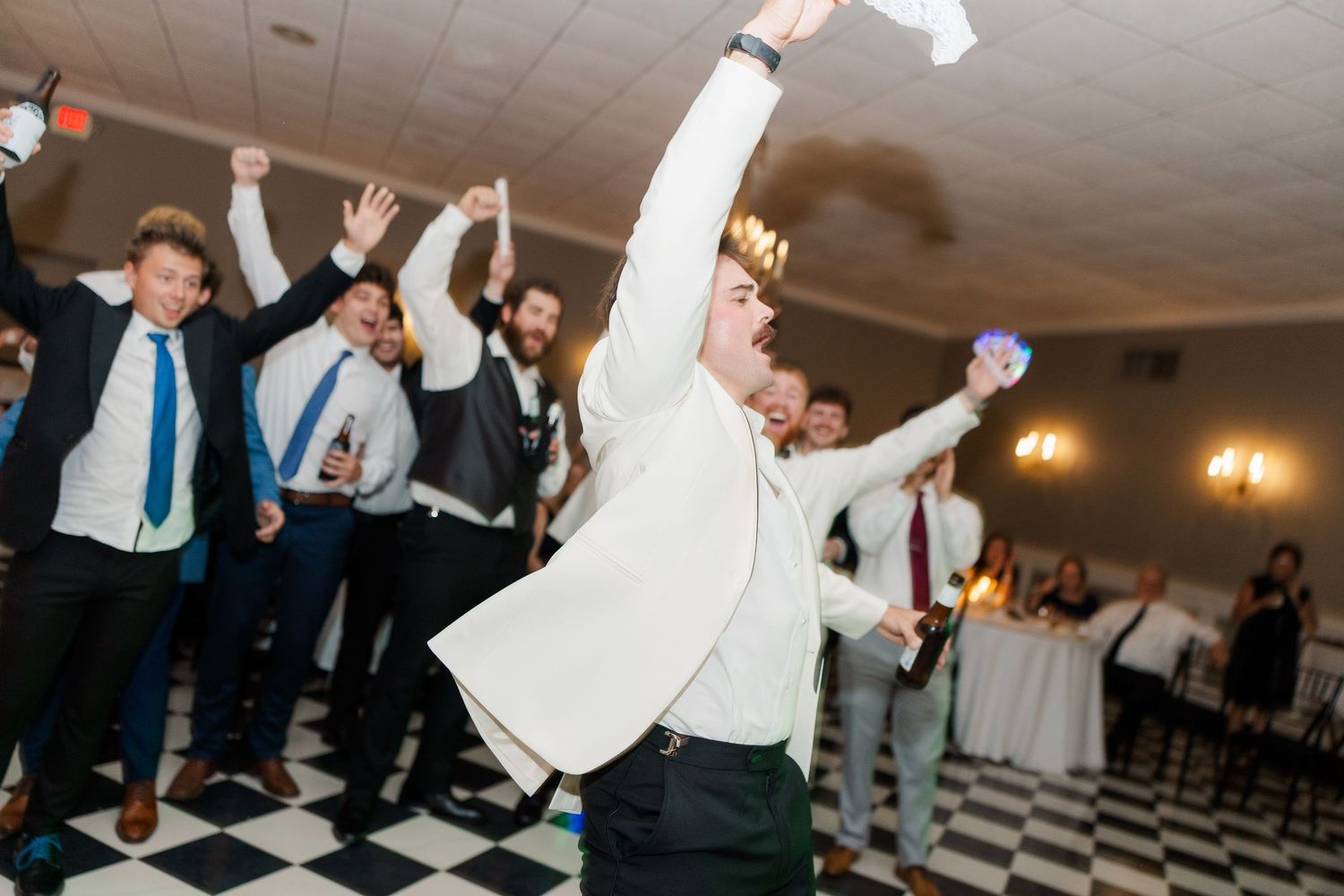 Wedding reception guests dancing and celebrating on checkered dance floor.