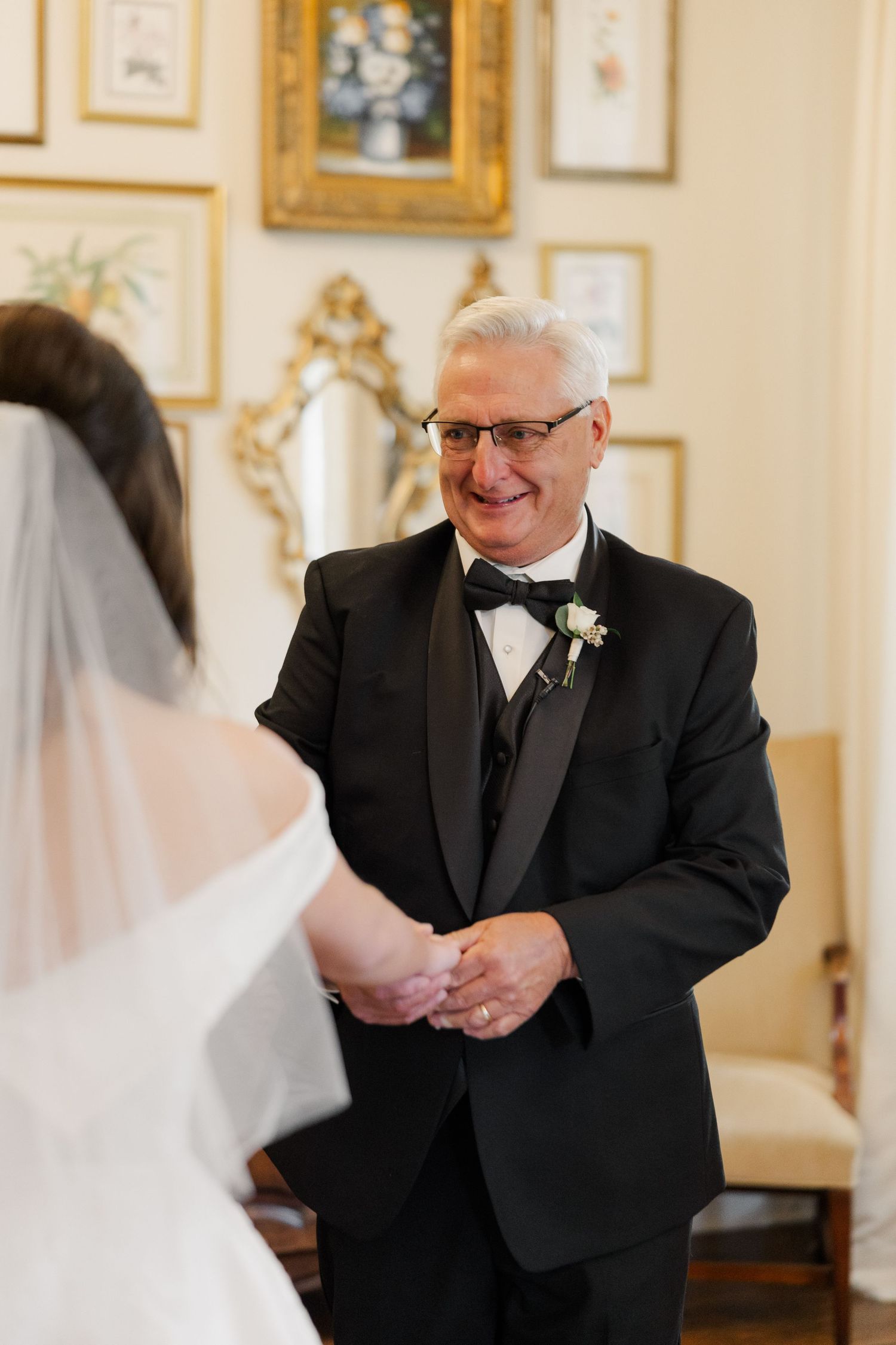 Emotional first look moment between bride and father in an elegant room with gold-framed artwork.