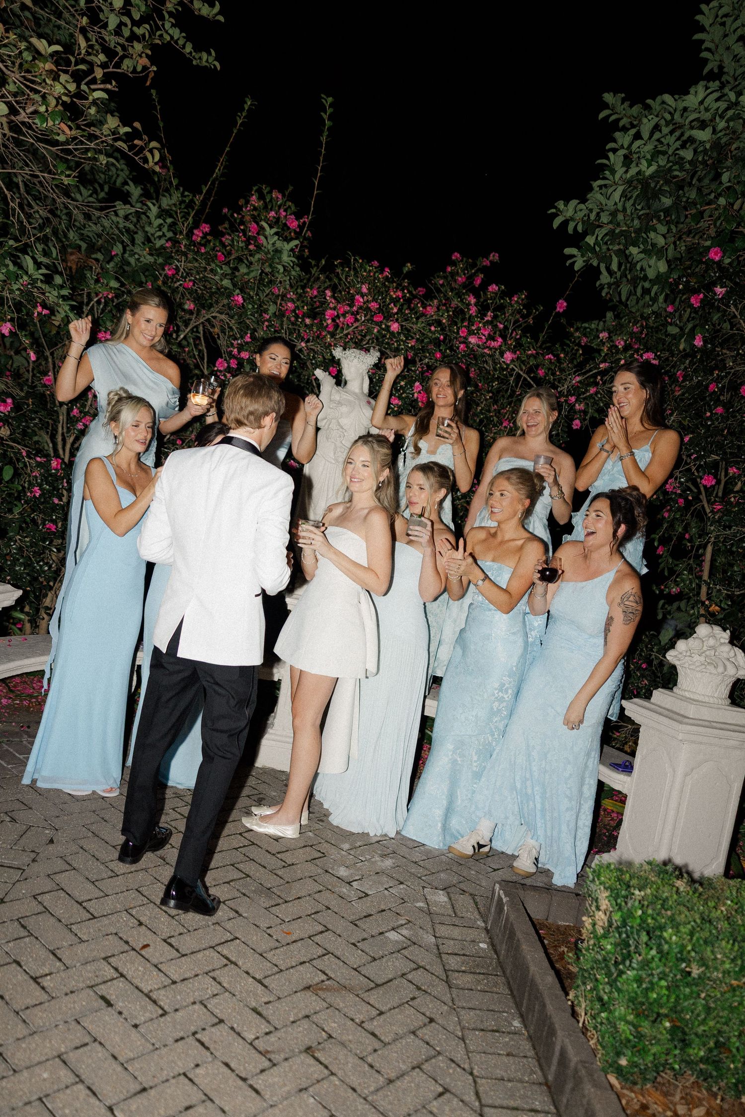 Wedding party in formal attire poses for fun group photos on an outdoor patio at night.