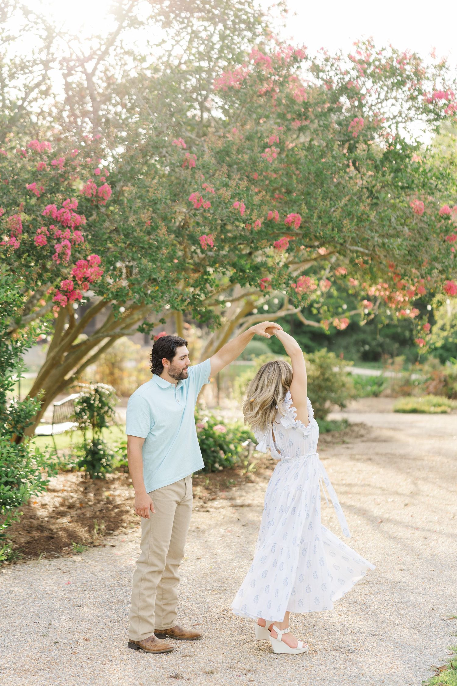 A couple dances together under blooming pink crepe myrtle trees in a romantic outdoor setting.