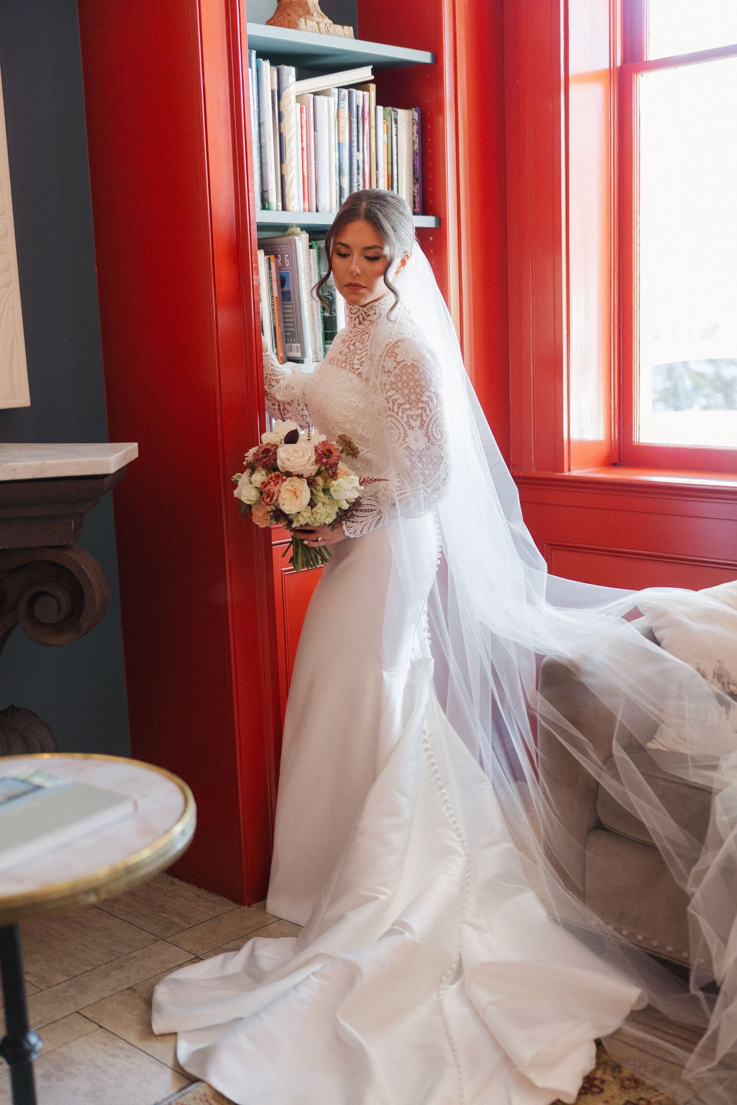 Bridal portraits in a room with red walls showing the flowing white wedding dress and veil details.