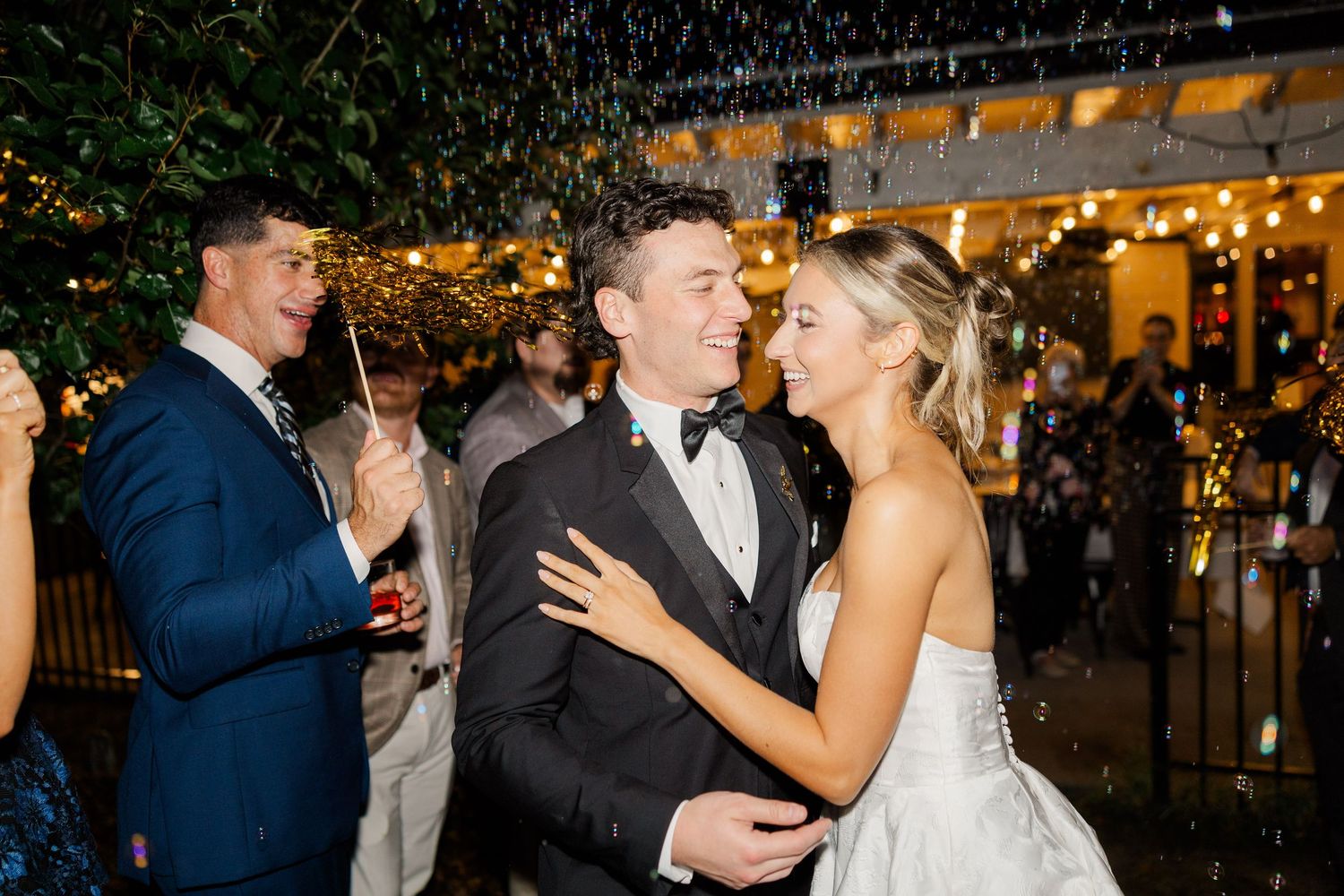 Wedding couple celebrates under string lights during evening reception festivities.