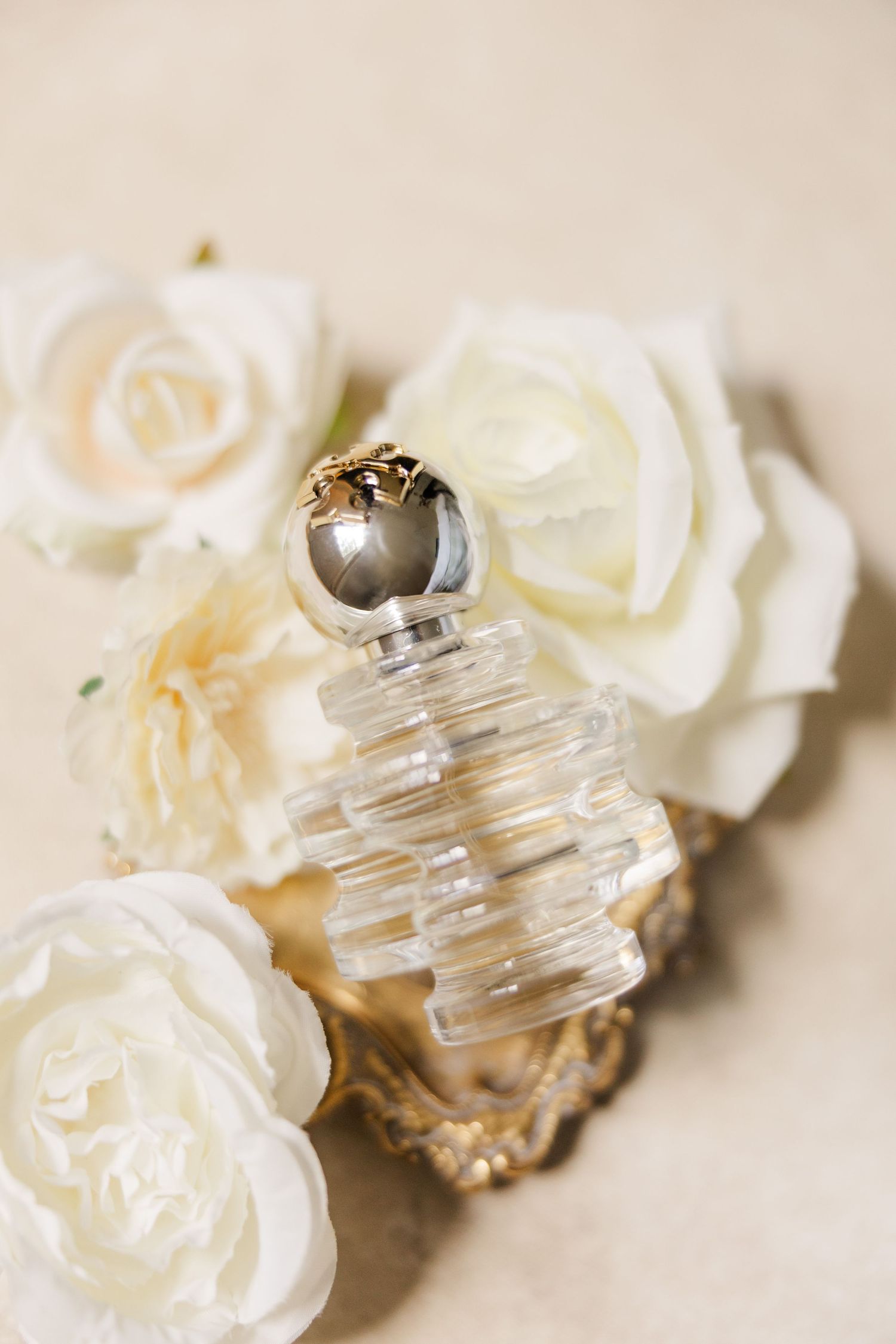 Close-up of vintage perfume bottles and white roses arranged for wedding details photography.