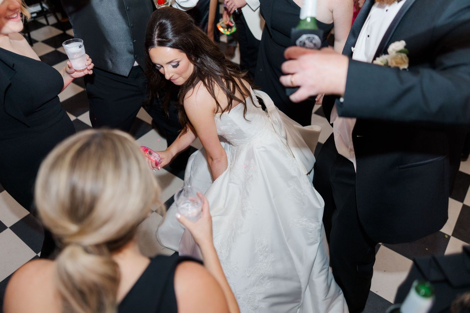 Wedding celebration with guests dancing energetically on checkered ballroom floor.