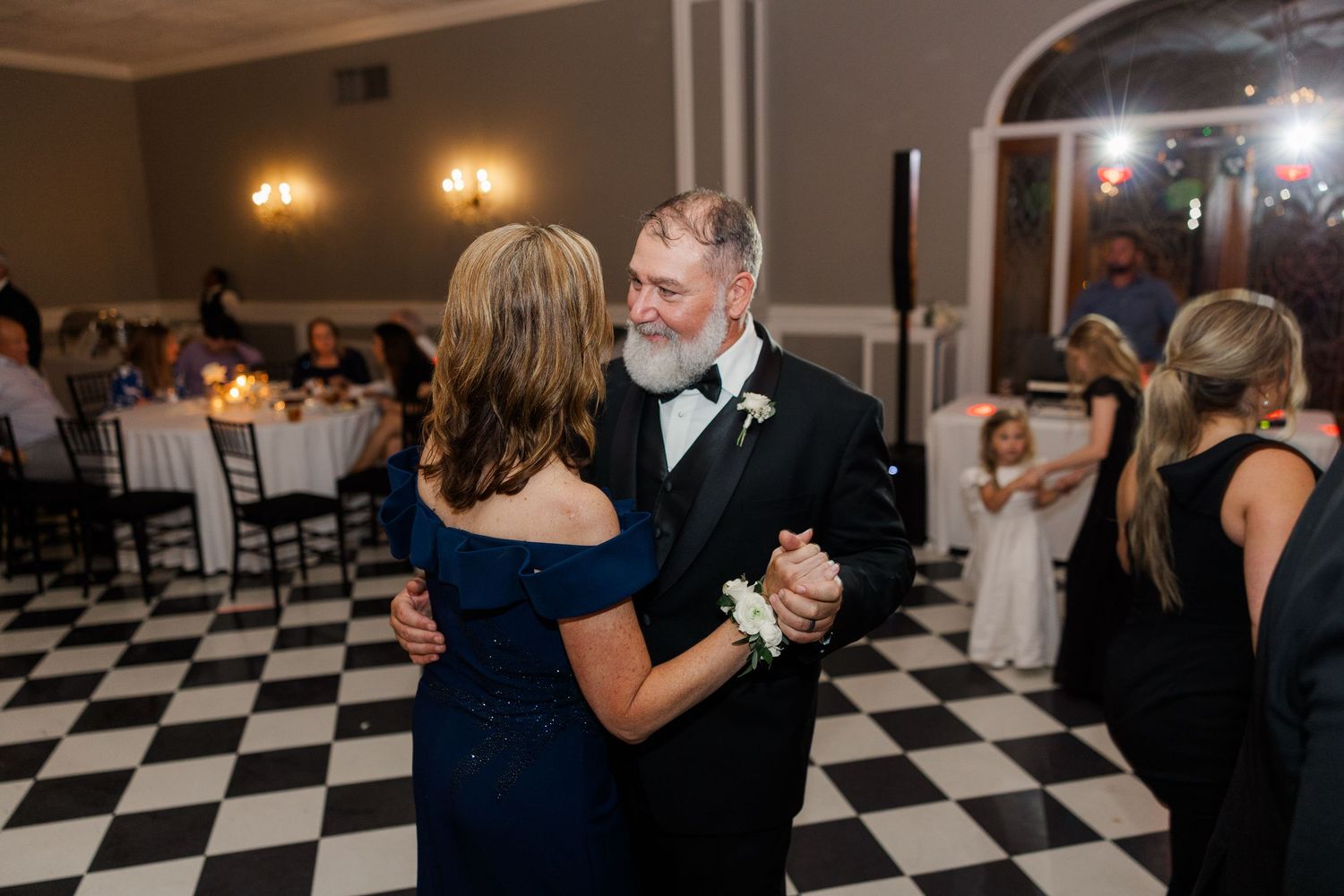 Couples dancing together on a black and white checkered ballroom floor at an elegant wedding reception.