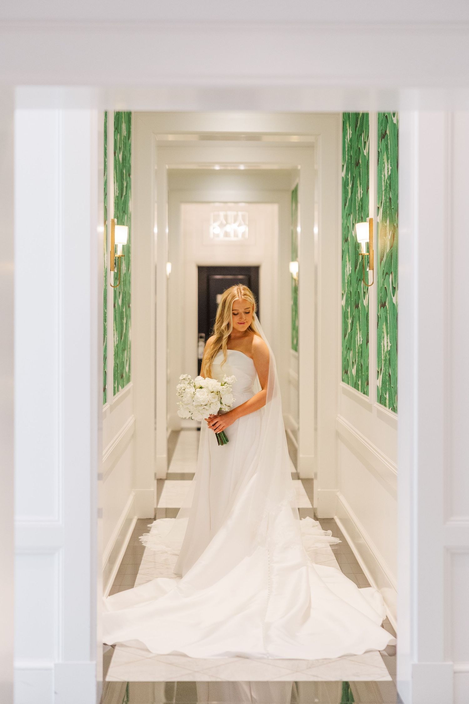 White wedding dress with long train displayed in an elegant hallway with green accents.