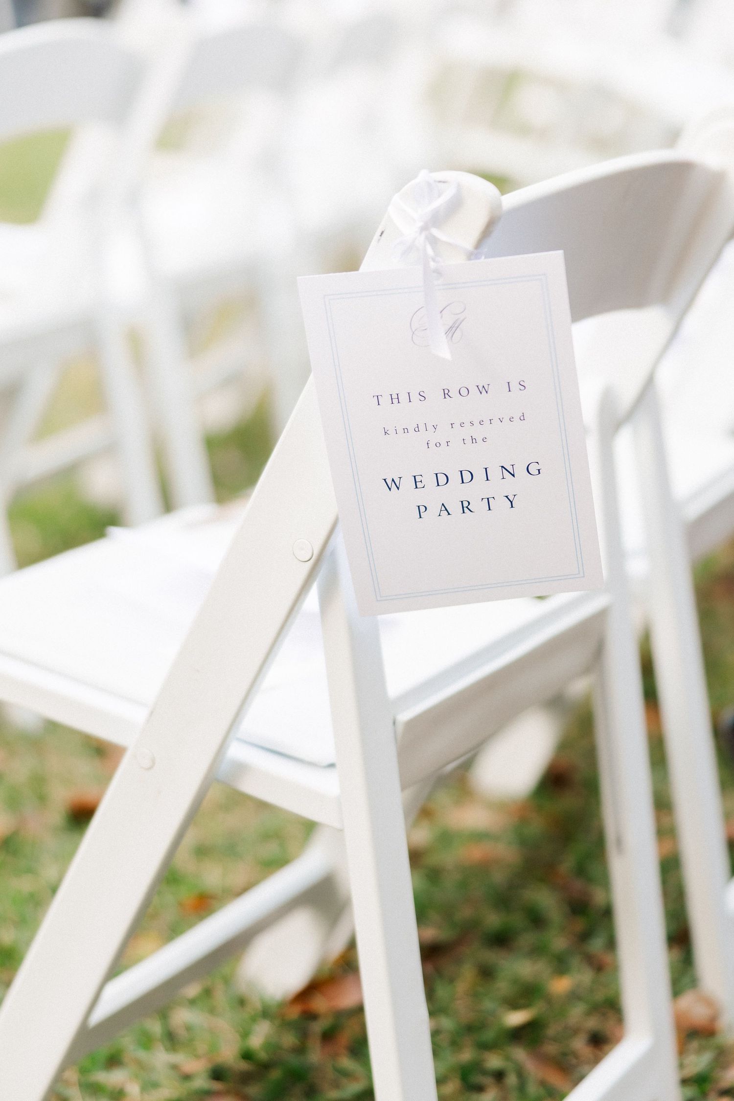 Row of white wooden ceremony chairs with reserved seating signs on grass.
