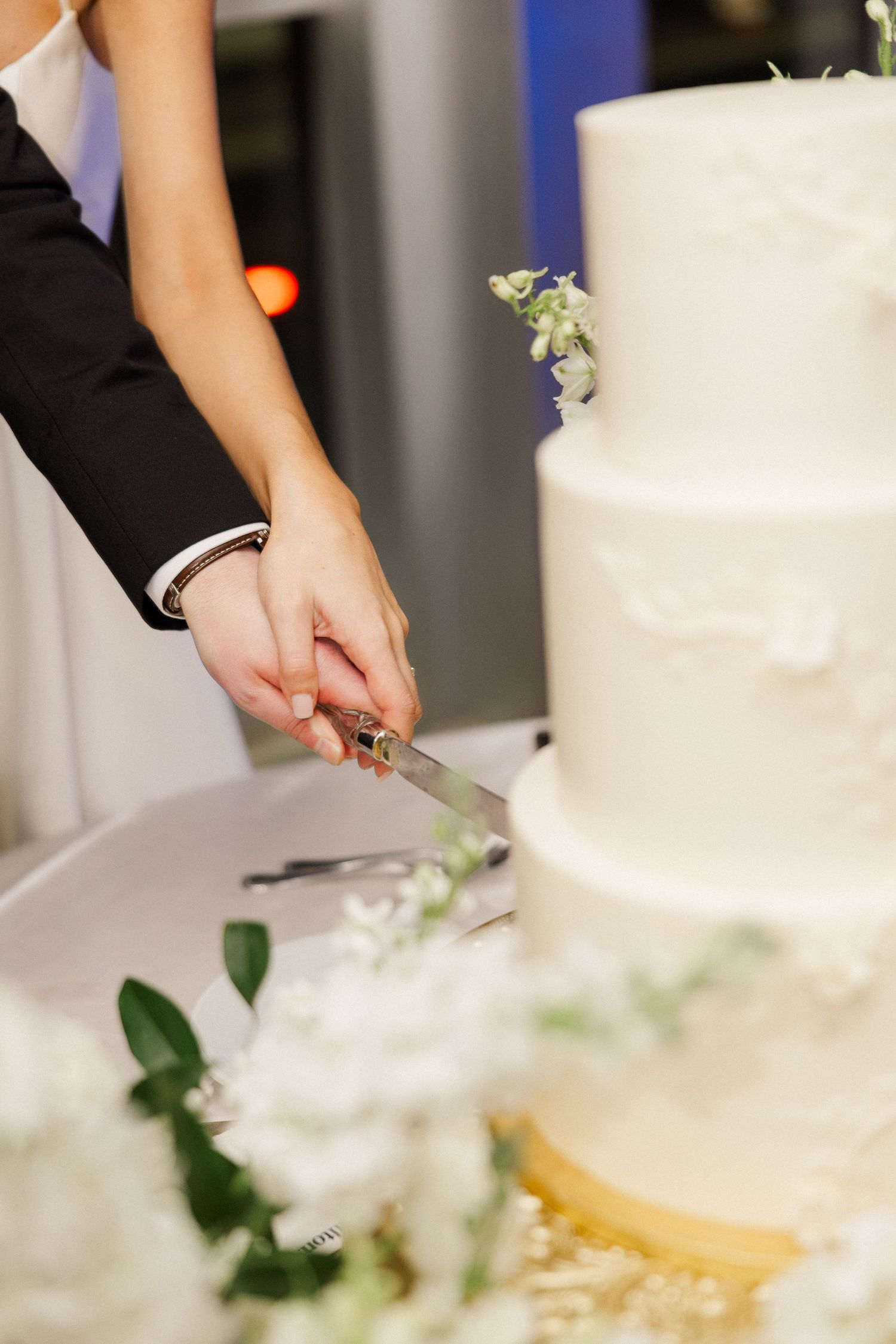 Bride and groom cut elegant white tiered wedding cake adorned with delicate flowers.