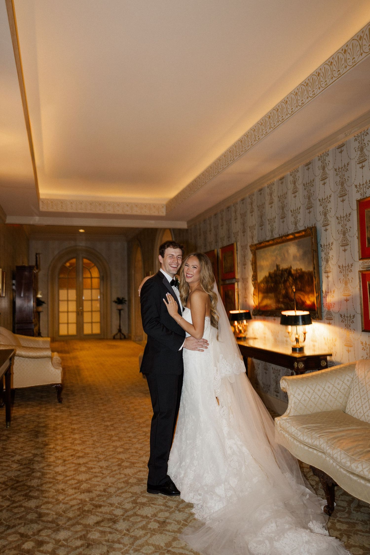 Elegant couple dancing in ornate hallway with patterned carpet and wallpapered walls.