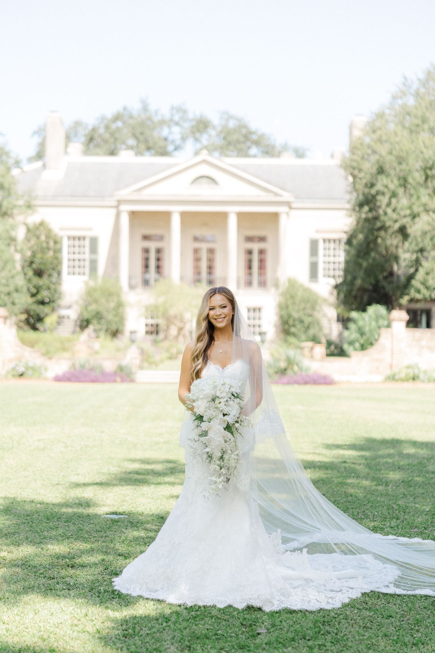 Dreamy bridal portrait on mansion lawn with neoclassical architecture in soft sunlight.