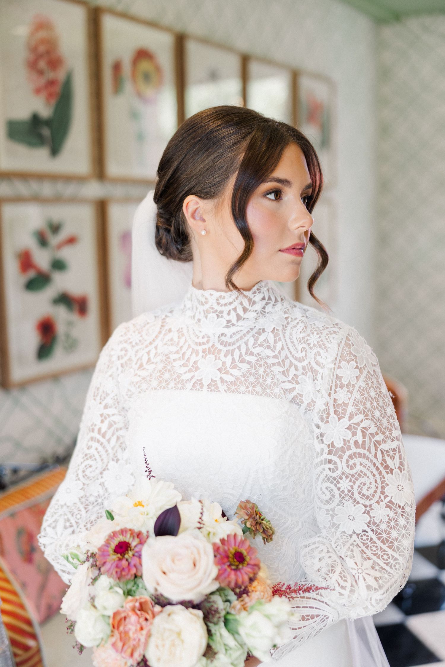 A bride in a lace-detailed wedding dress holds a romantic bouquet of pink, peach and white flowers.