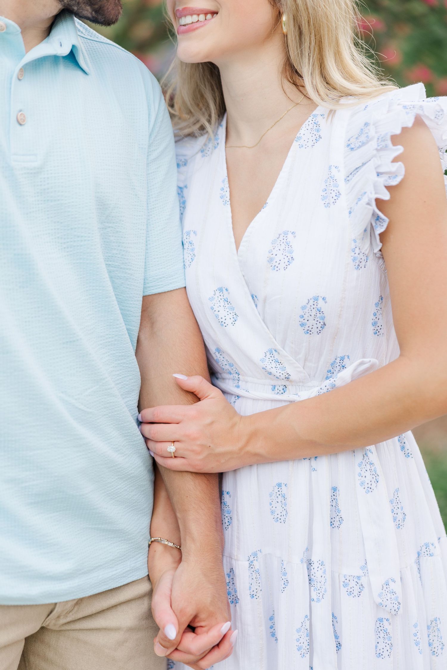 Close-up of couple holding hands, with her wearing a white floral dress and him in a light blue polo shirt.