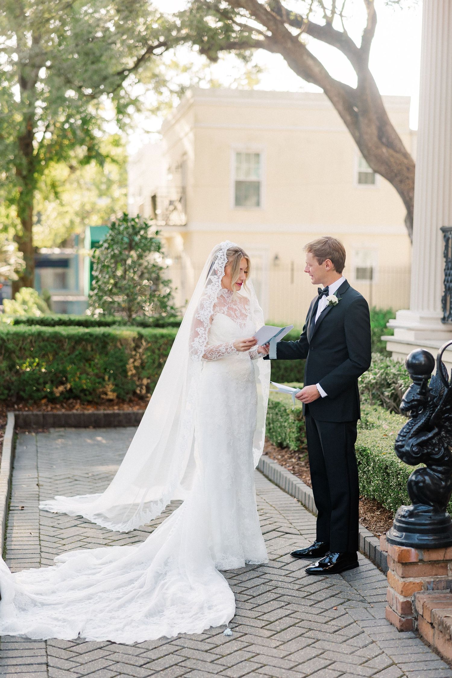First look wedding moment on brick patio with white columns and flowing veil.