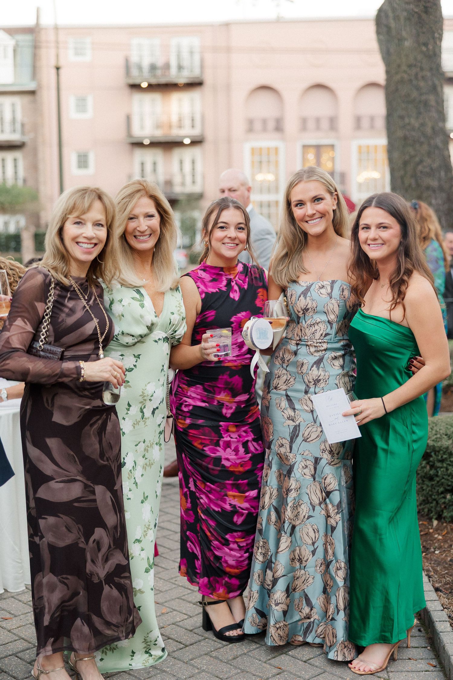 Group of wedding guests in colorful dresses pose together at an outdoor reception.